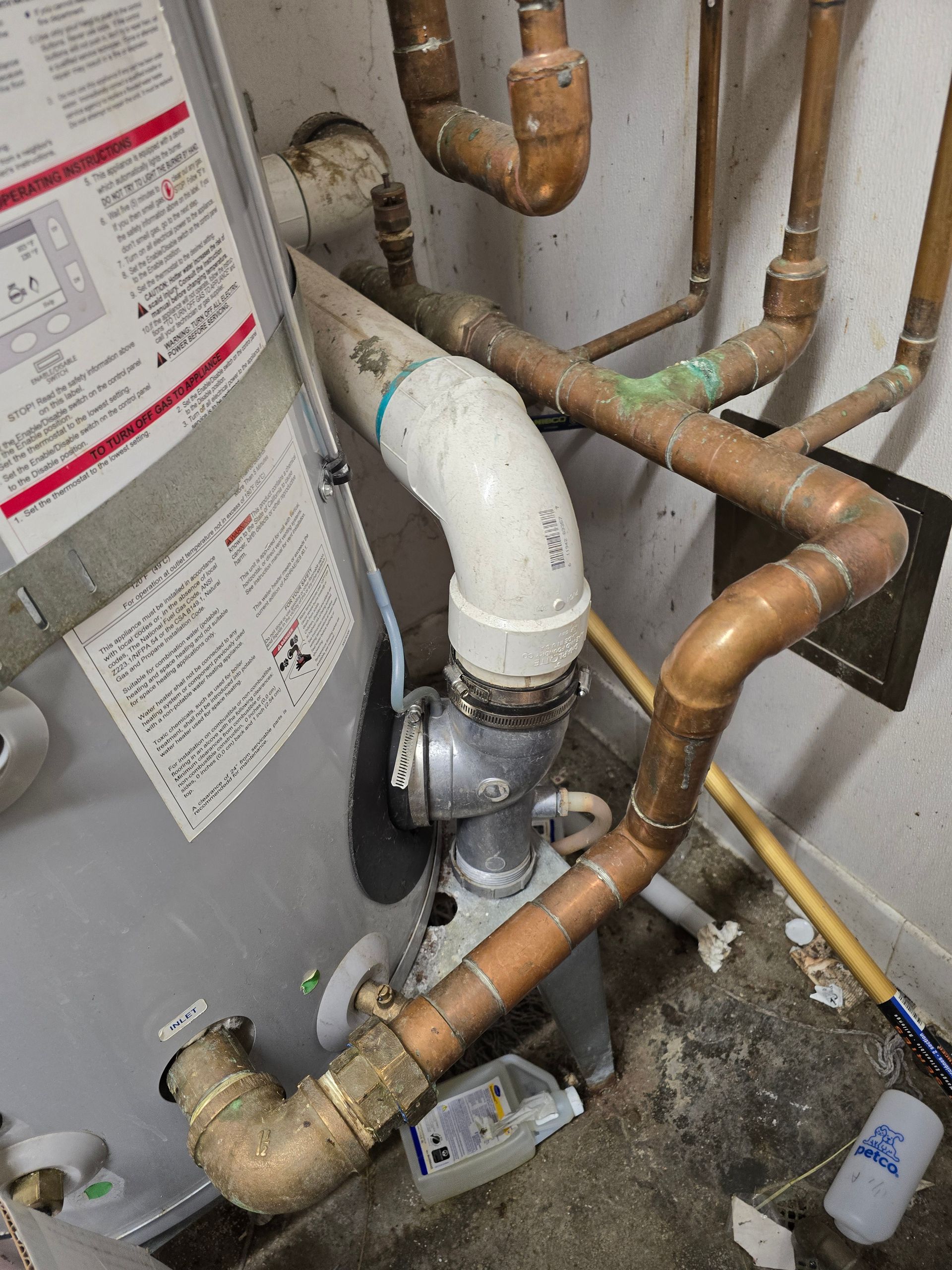 Water heater plumbing with copper pipes, white PVC vent, and a condensate pump in a utility closet