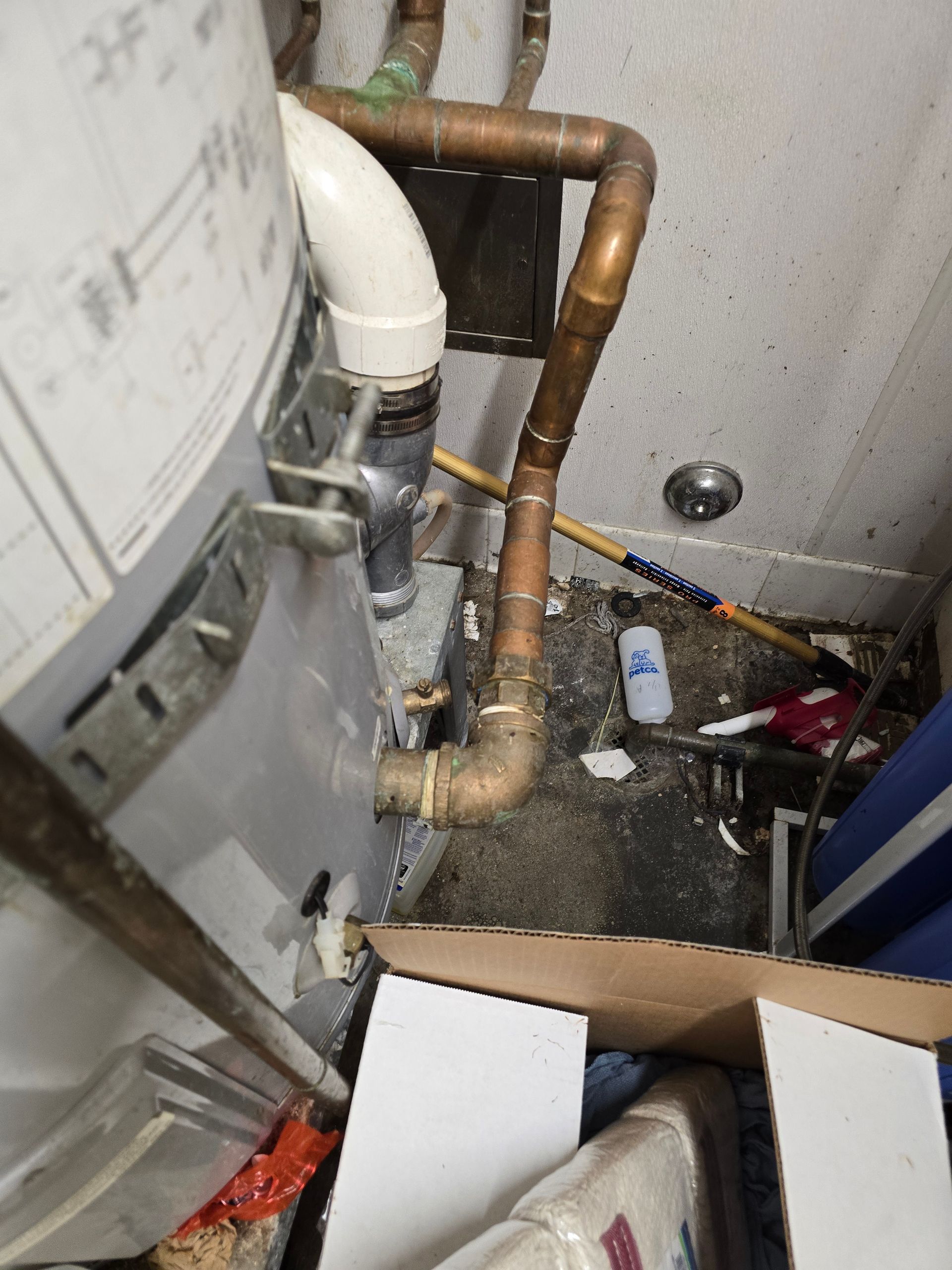 Plumbing and pipes beside a water heater in a utility closet, with a cardboard box on the floor.