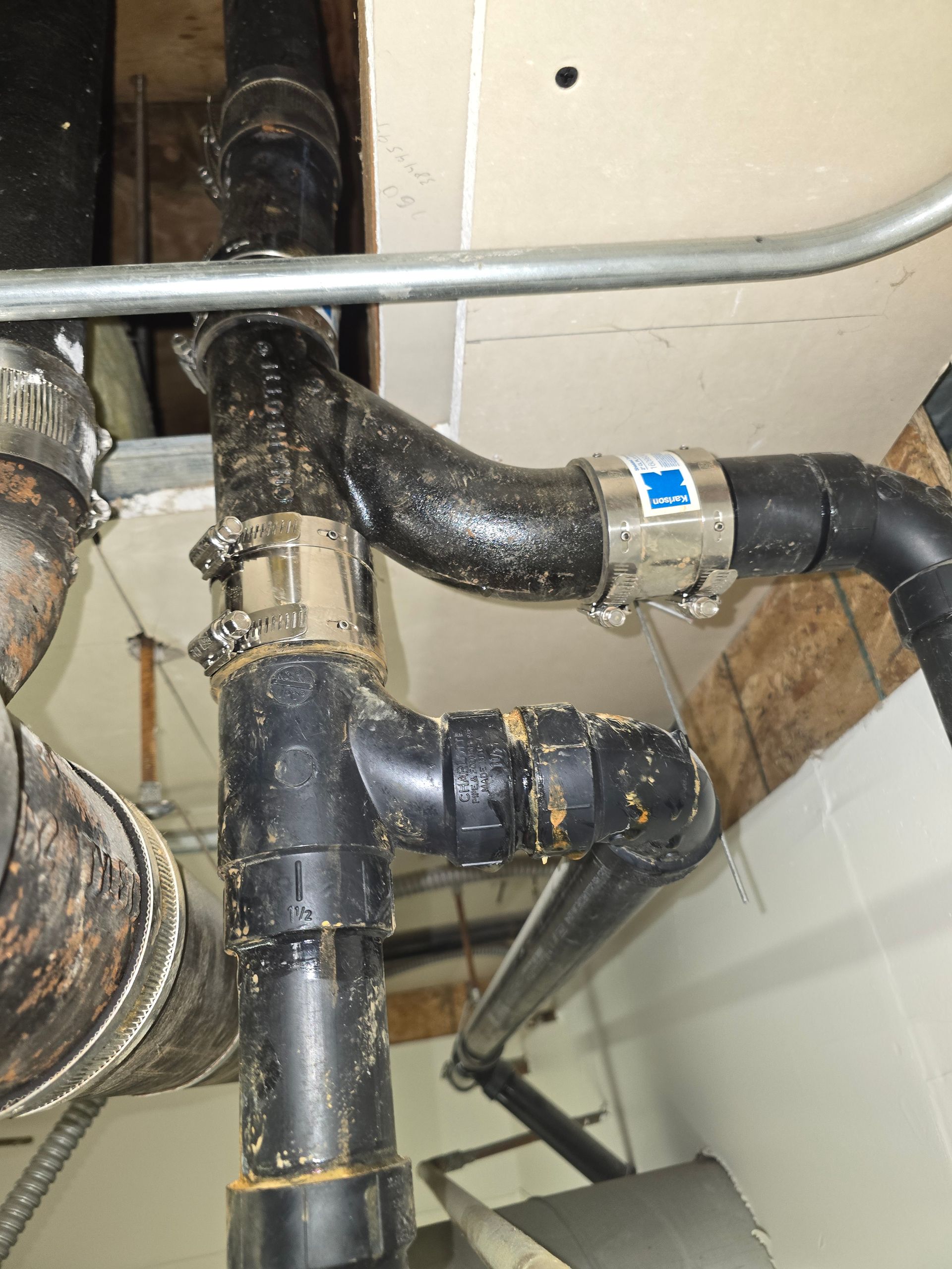 Black metal plumbing pipes with a silver clamp in a utility area underneath a sink.