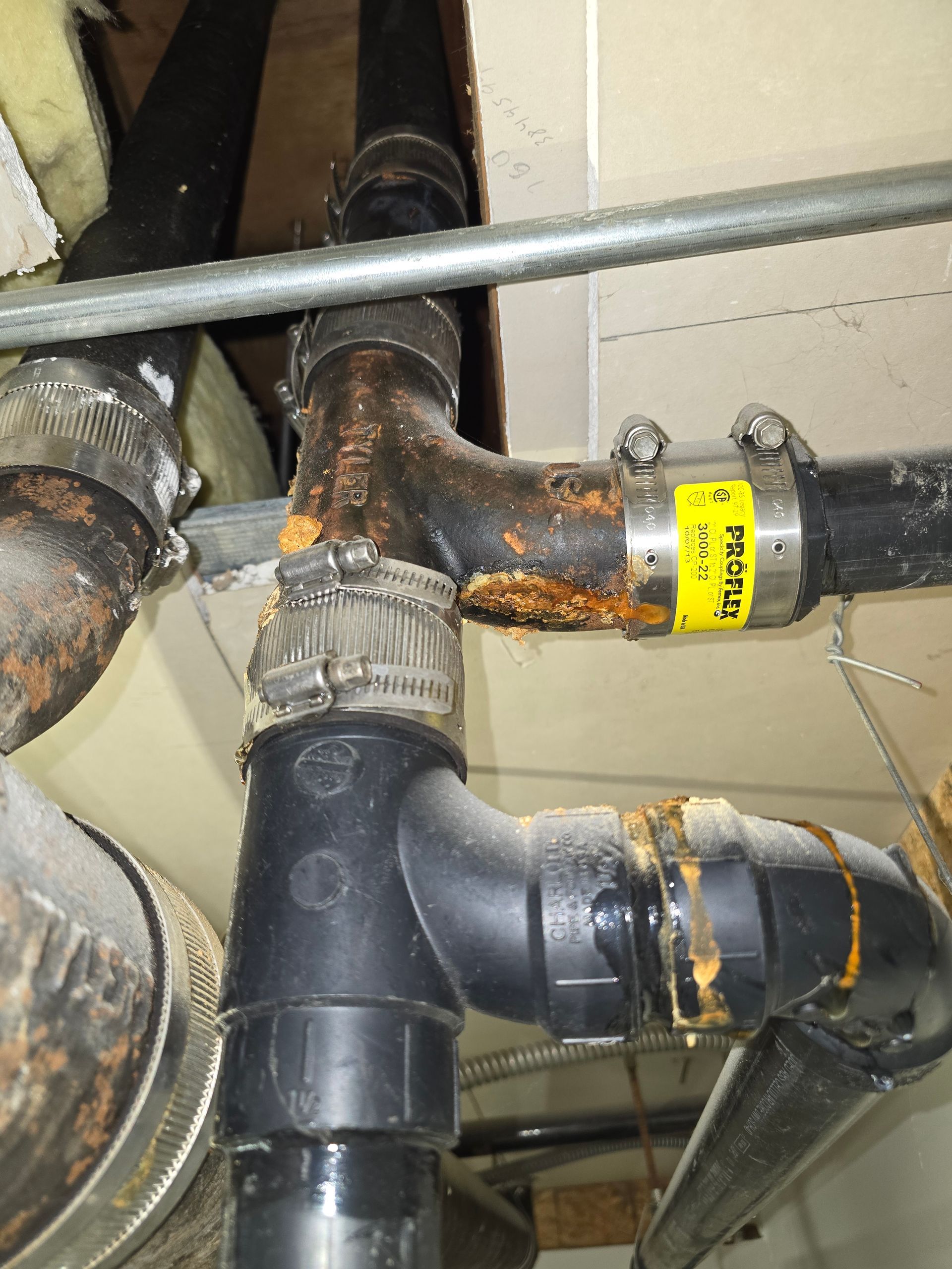 Corroded black plumbing pipes with rusted metal joints and a yellow label in a utility space