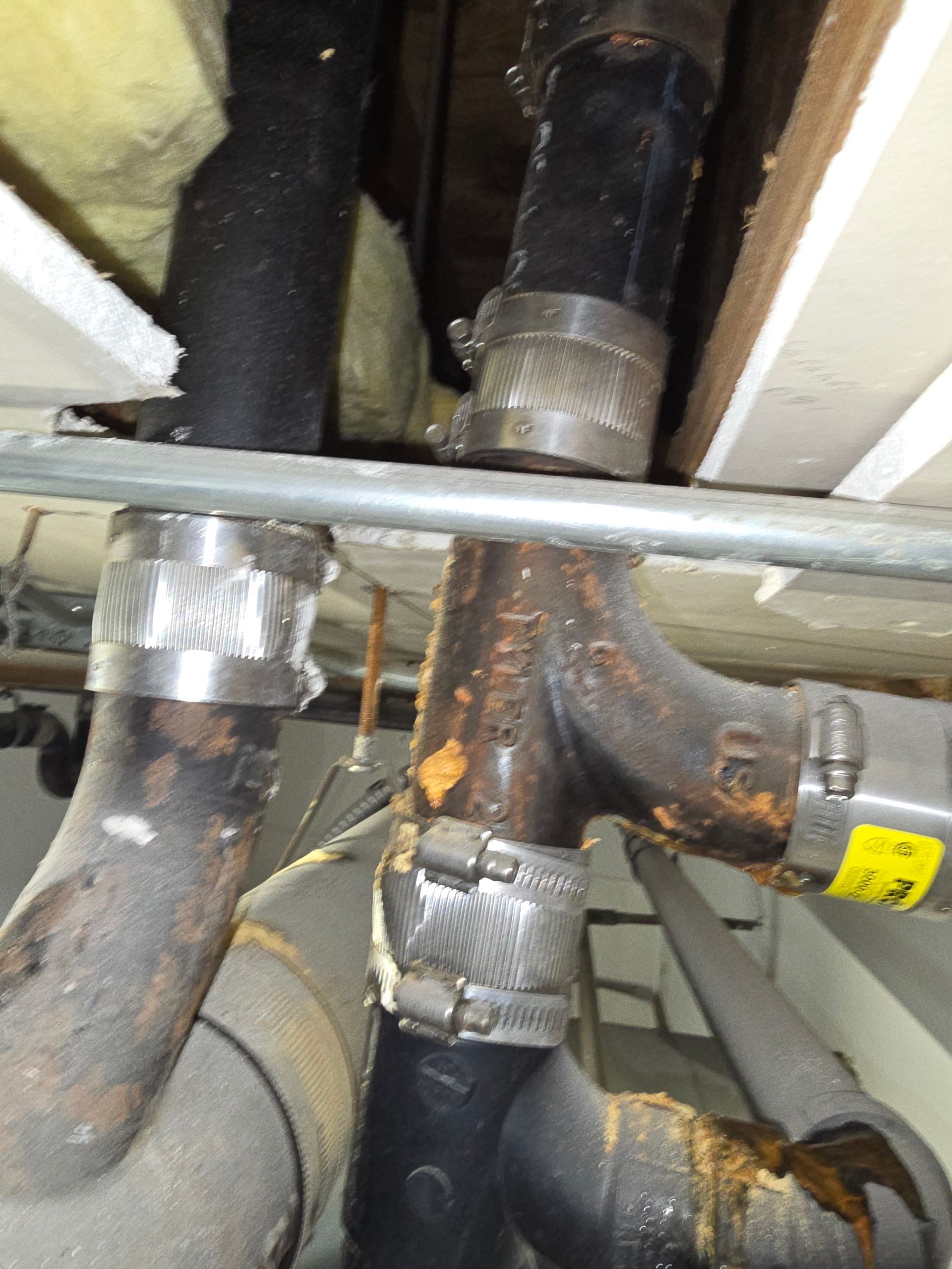 Corroded metal pipes and insulated plumbing joints under a sink or floor opening