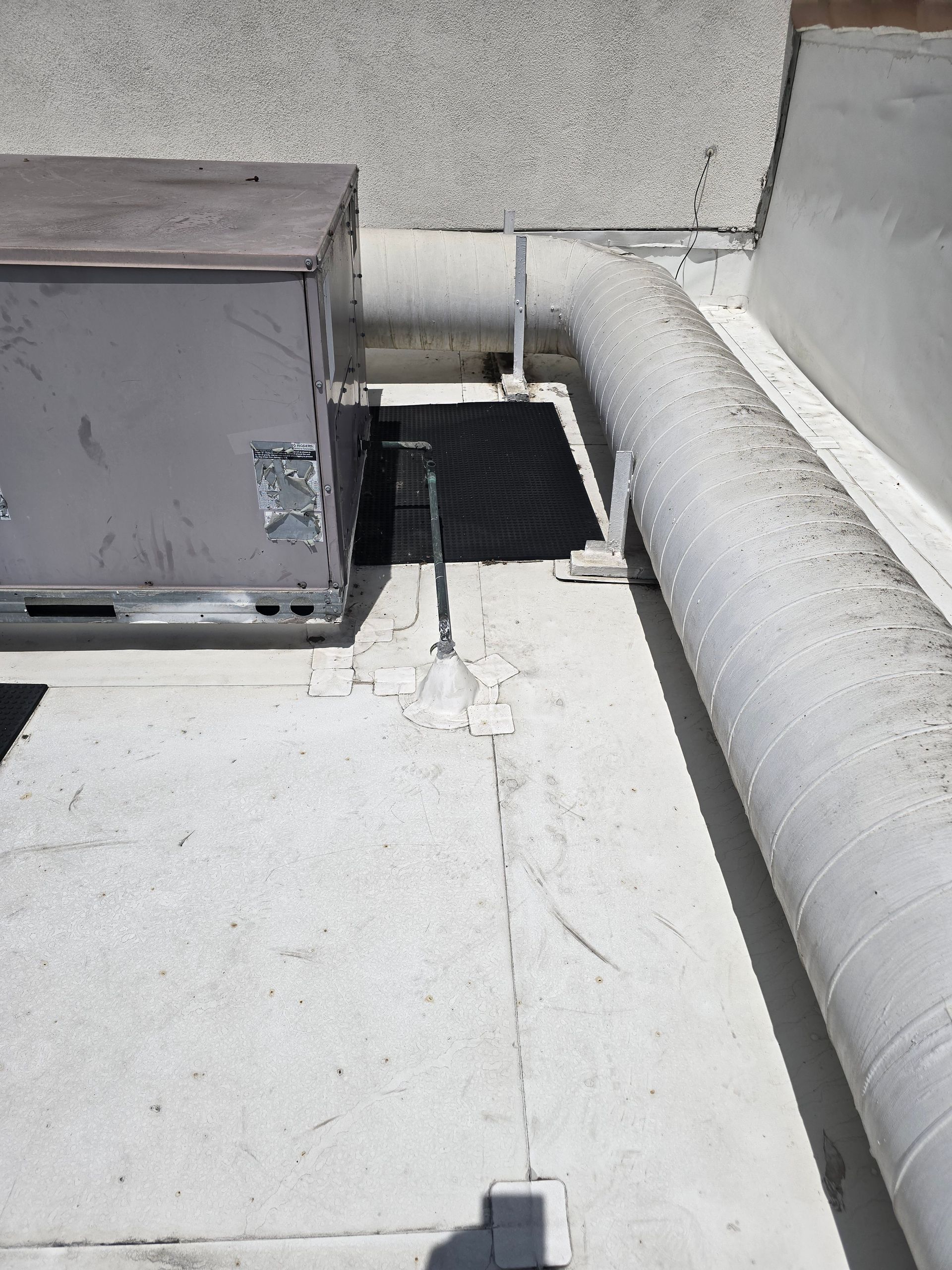 Rooftop HVAC unit with ducts and a black drain grate on a white roof.