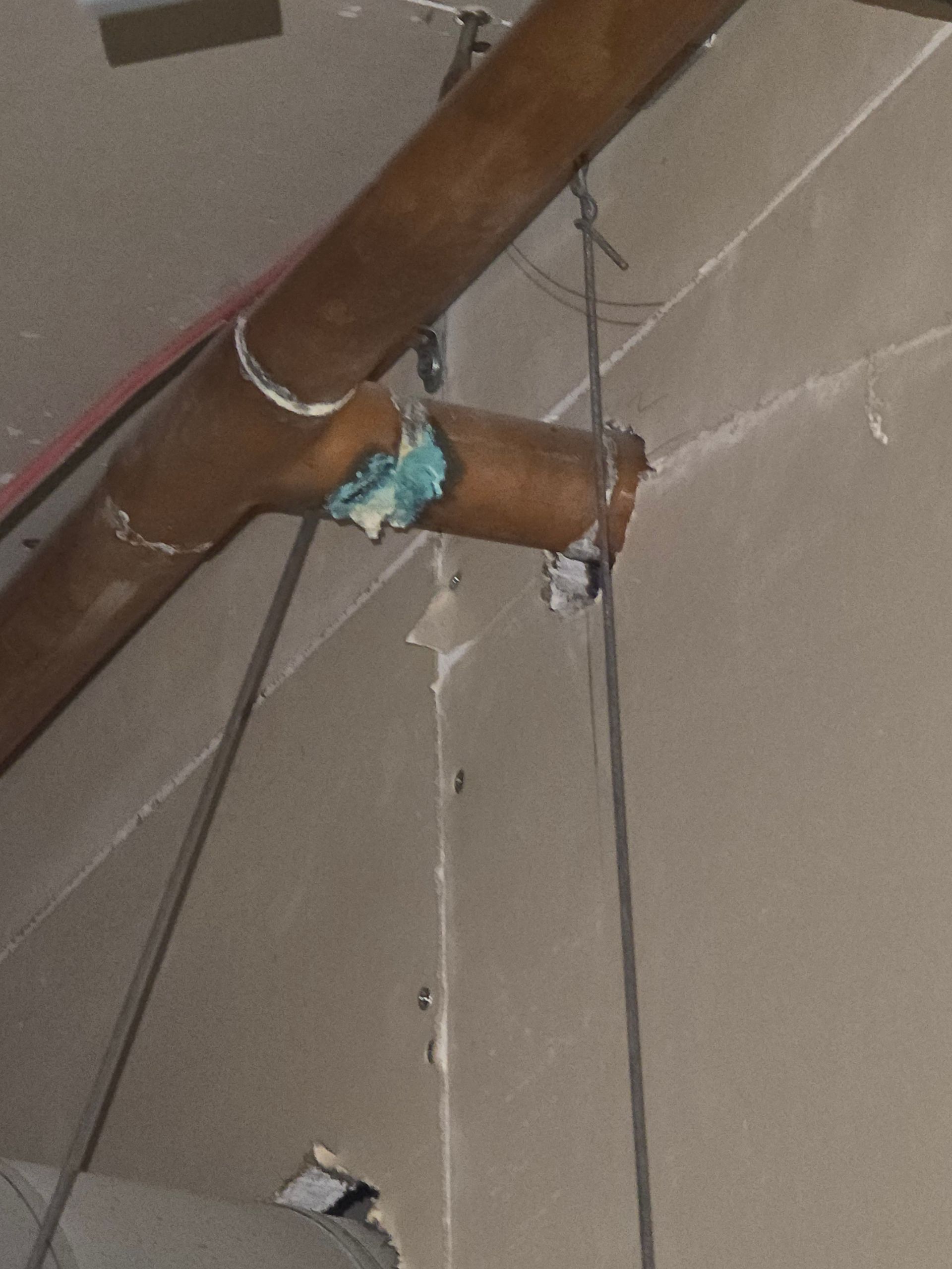 Exposed brown ceiling pipe with blue insulation hanging loose in a damaged indoor ceiling