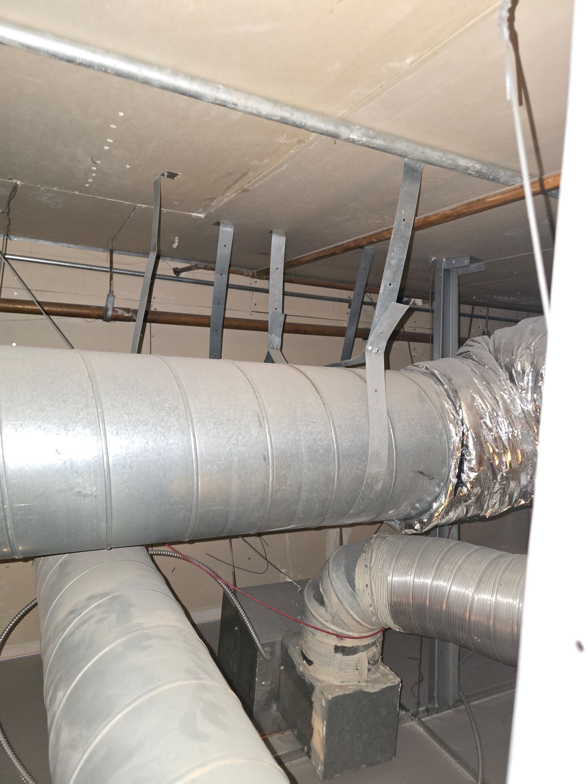 Large silver HVAC ducts and pipes in a dim utility space under a ceiling