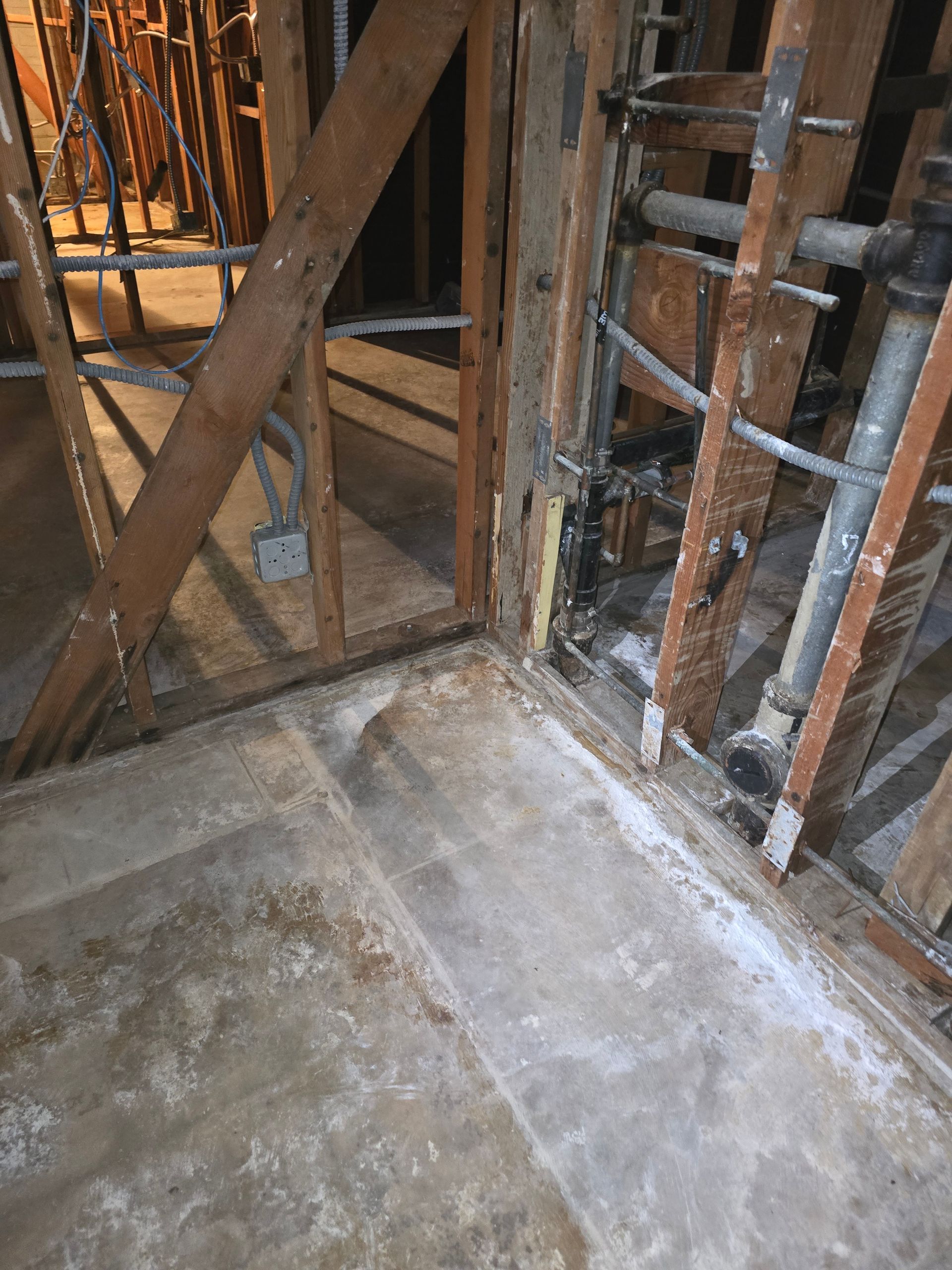 Construction framing inside a building corner with exposed wood studs and a concrete floor.