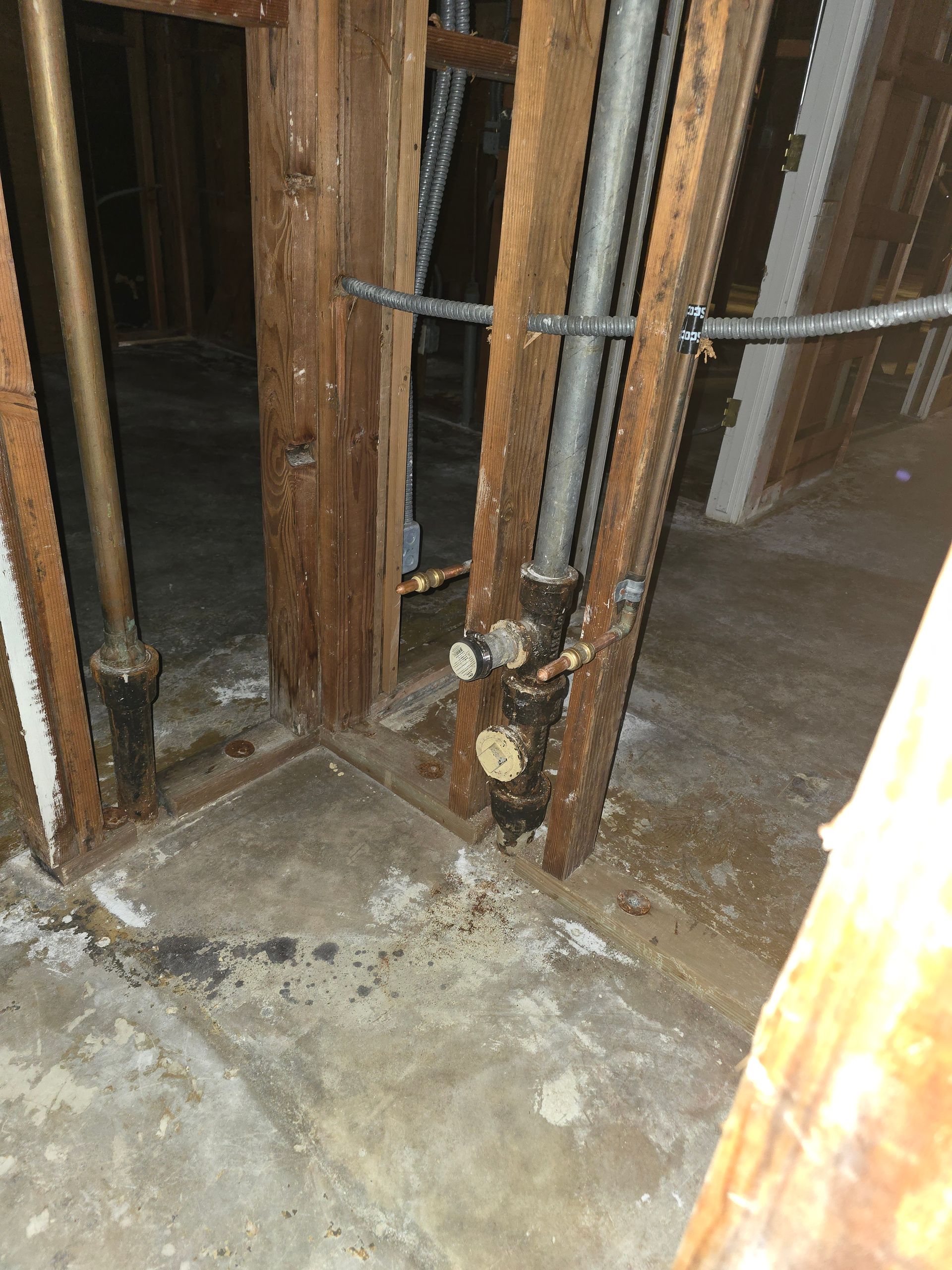 Damaged wooden framing and exposed pipes at a floor opening in an unfinished interior construction area