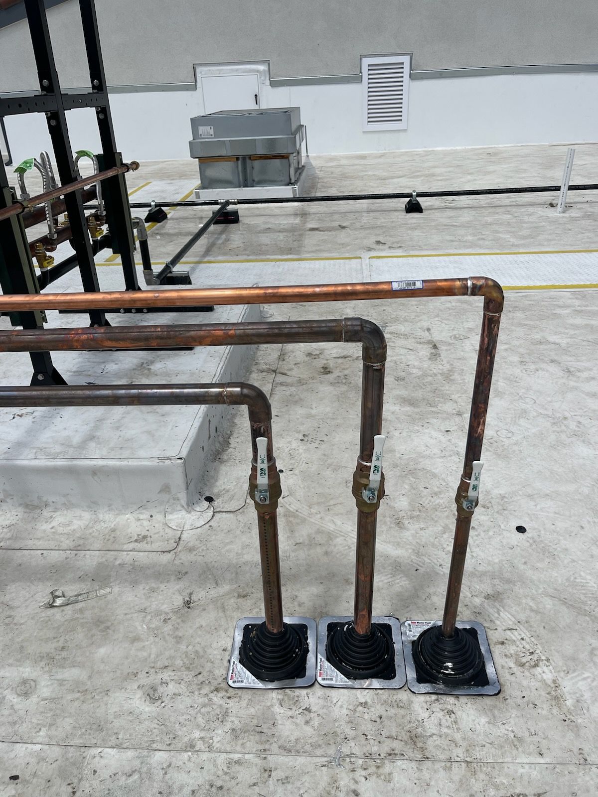 Three rusted metal pipes rising from black bases on a concrete rooftop near a wall.