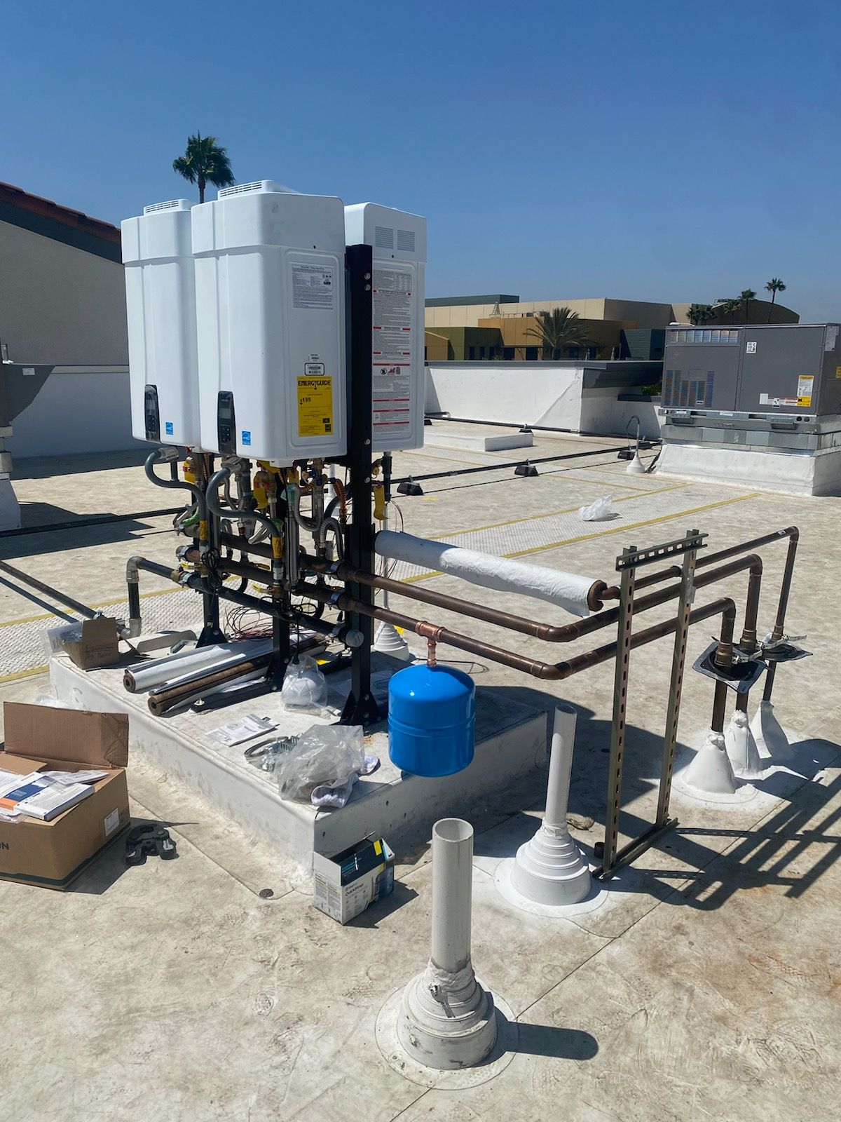 Rooftop HVAC unit with exposed copper piping, blue tank, and white vent pipes on a flat roof
