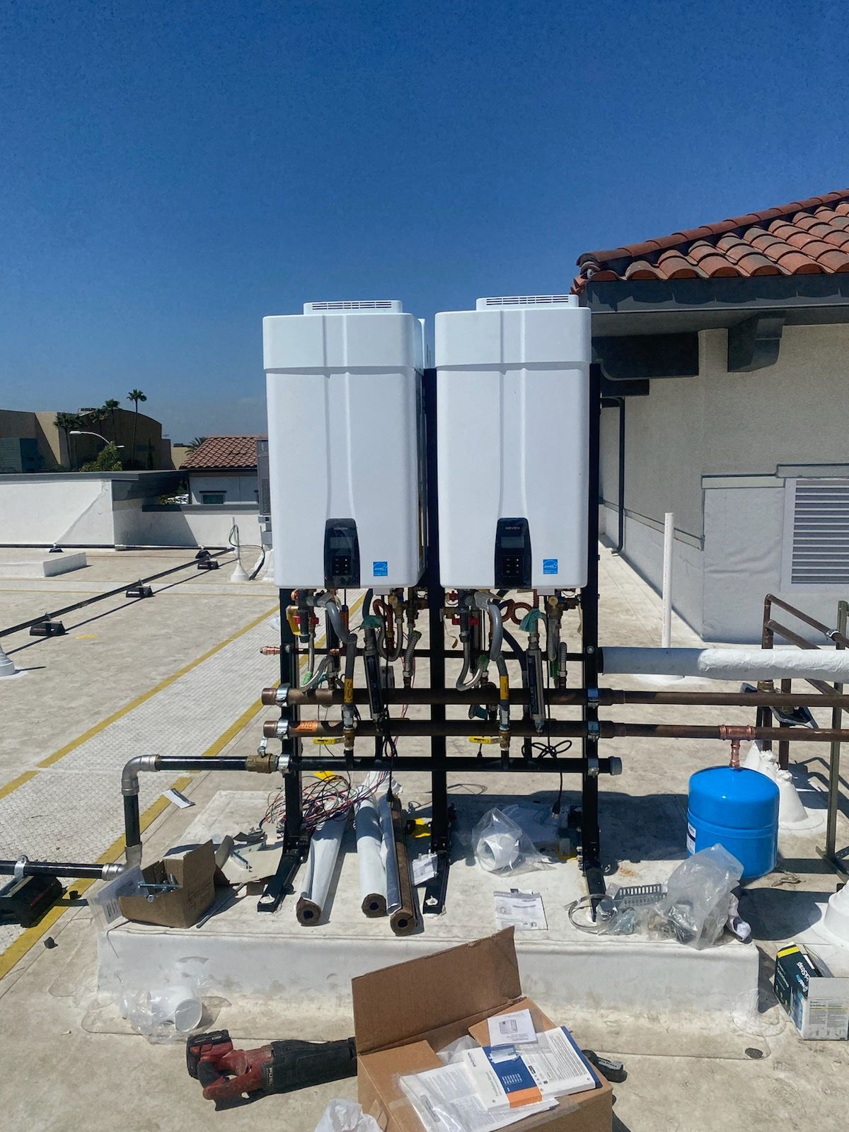 Rooftop with two white water tanks, pipes, and plumbing equipment under a clear blue sky.