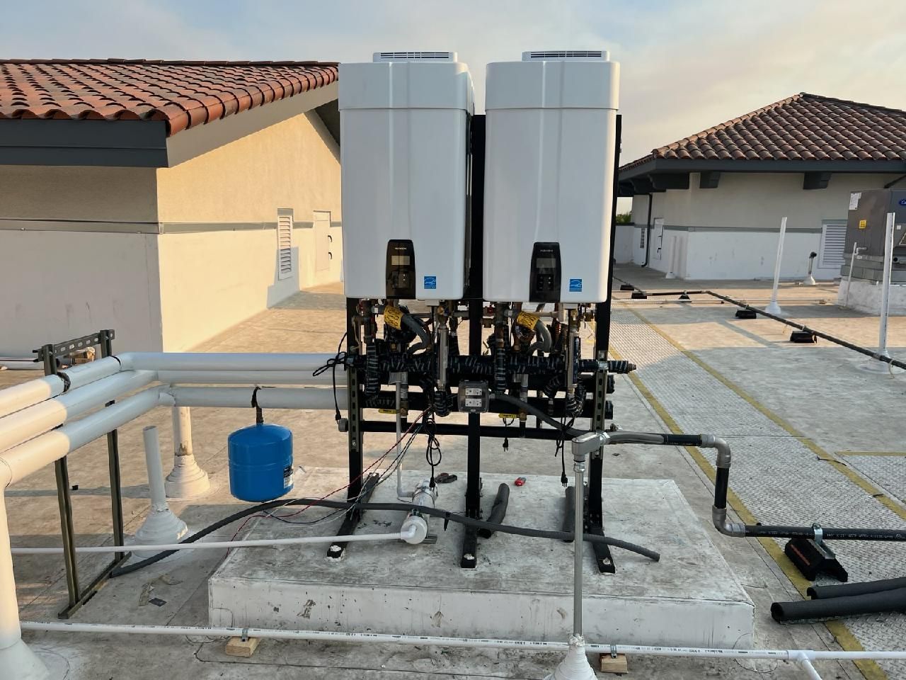 Outdoor rooftop mechanical equipment with two white tanks and piping on a concrete platform