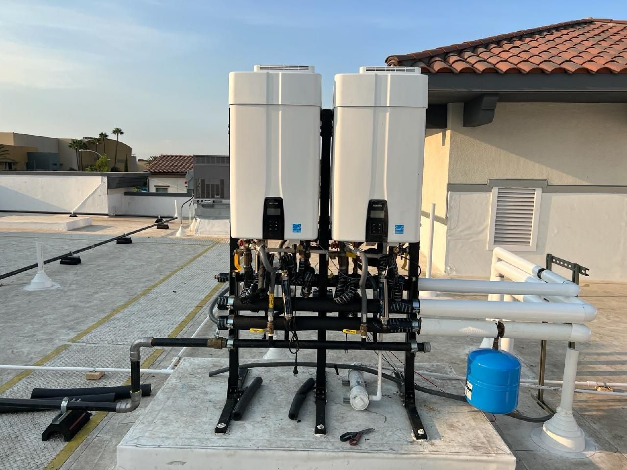Outdoor rooftop water filtration system with two white tanks, black piping, and a blue container beside pipes