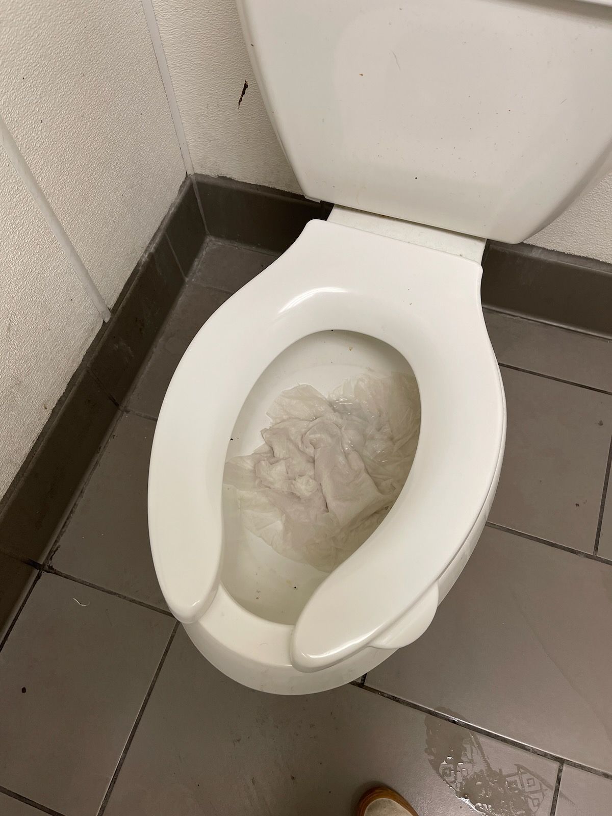 Toilet with an open seat, containing crumpled paper, in a bathroom corner.