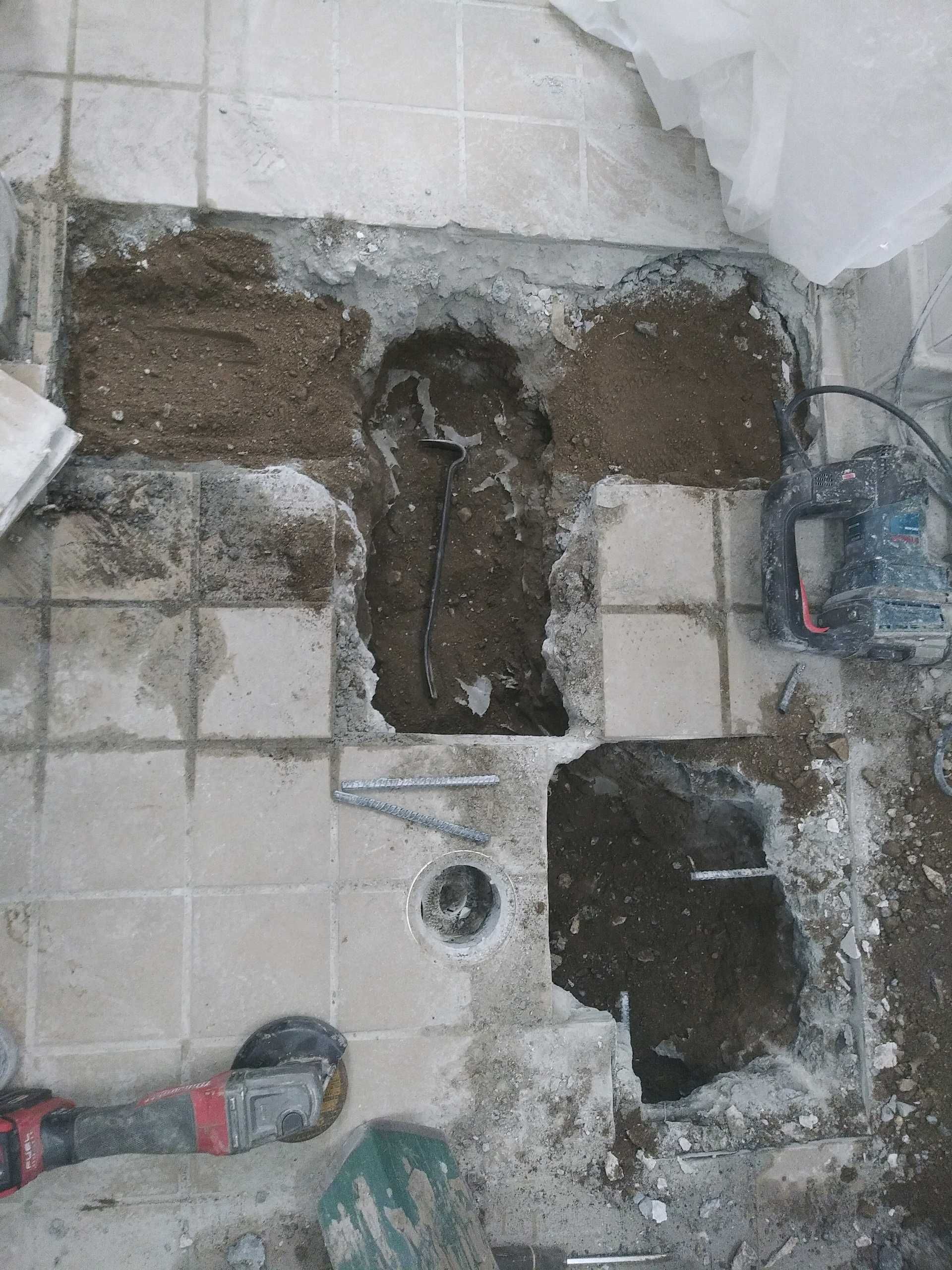 Bathroom floor with removed tiles exposing rough subfloor and a drain hole