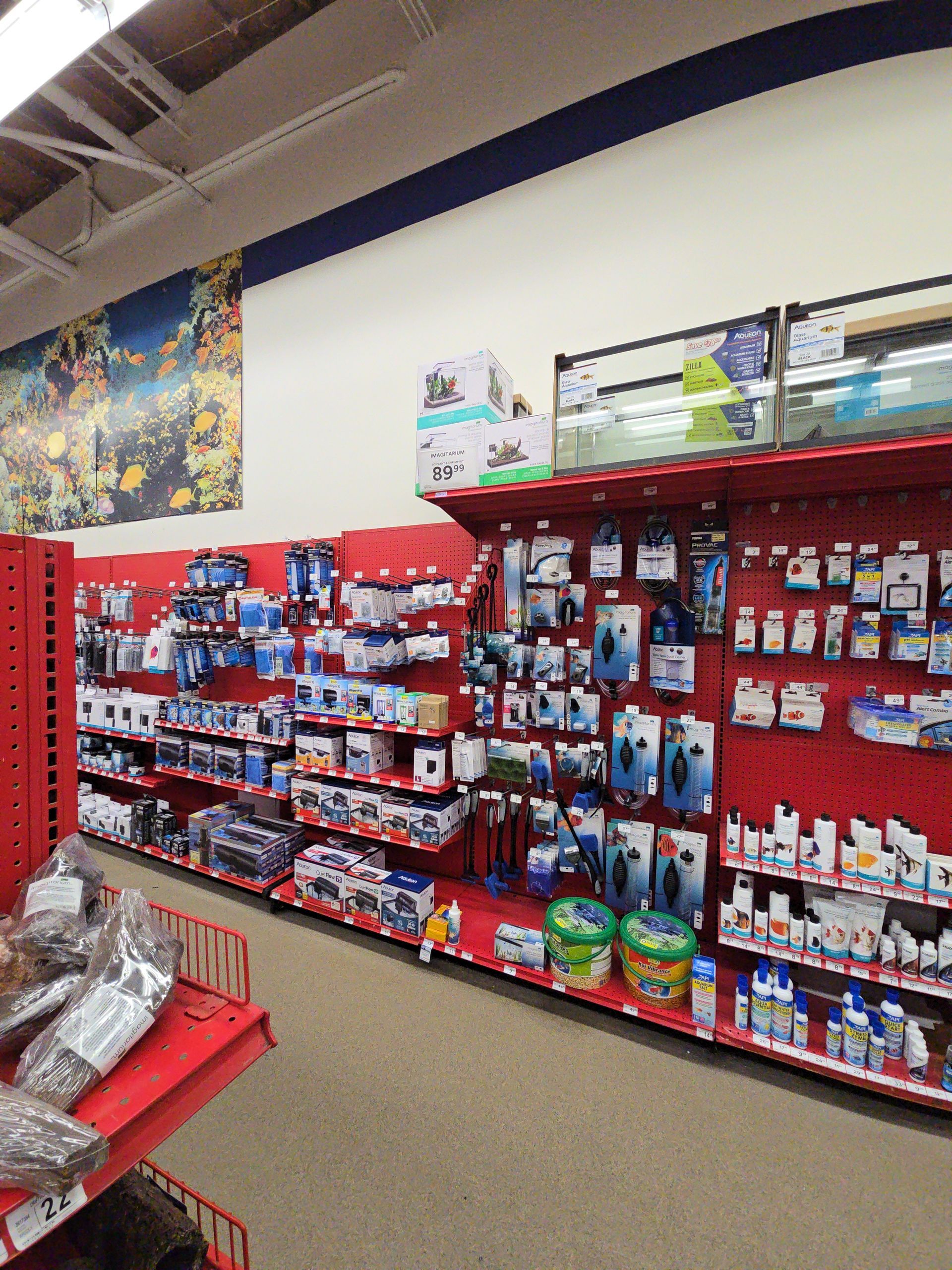 Store aisle with red shelving stocked with small pet and hardware items, viewed at a slight angle.