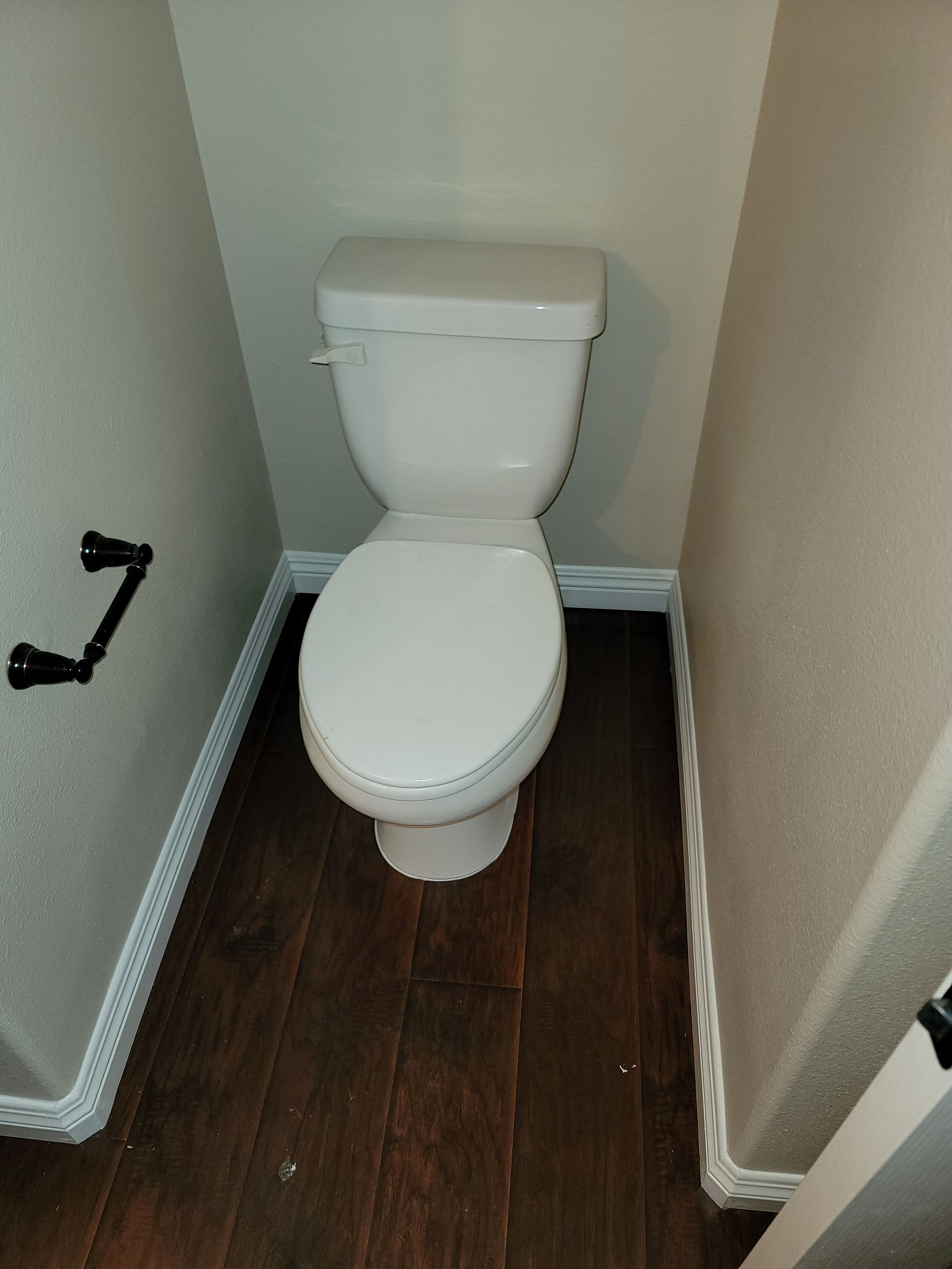 Small toilet in a narrow bathroom with beige walls and dark wood flooring.