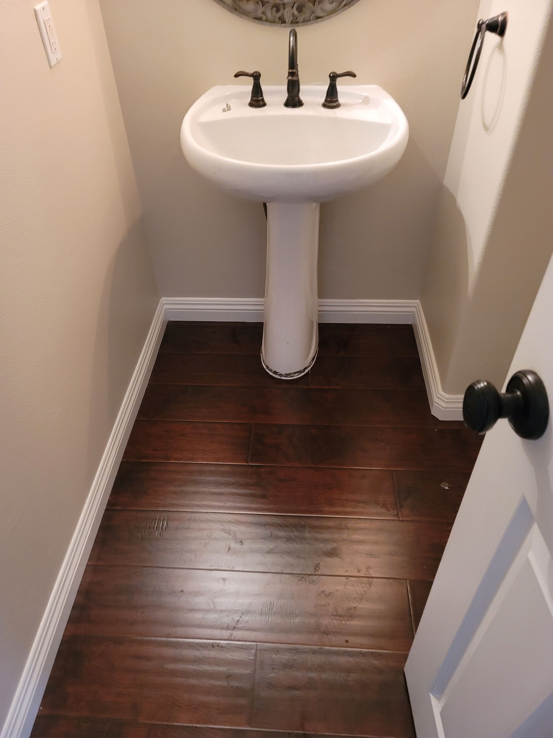 Small narrow bathroom with a white pedestal sink and dark wood floor.