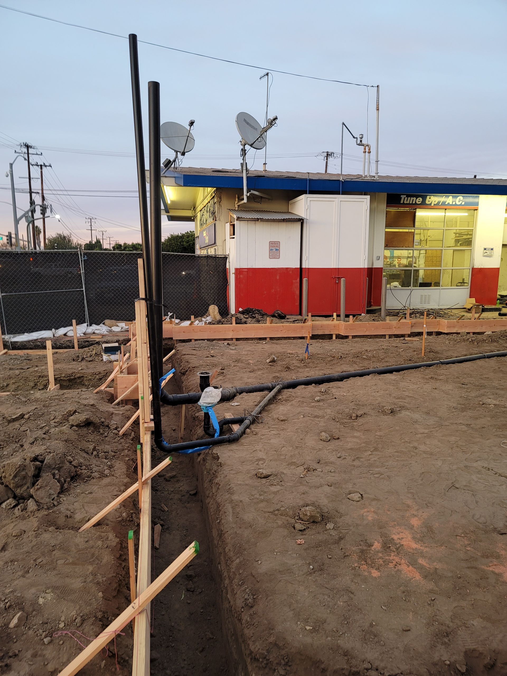 Small roadside building with blue roof and solar panels at dusk, surrounded by dirt and utility poles.