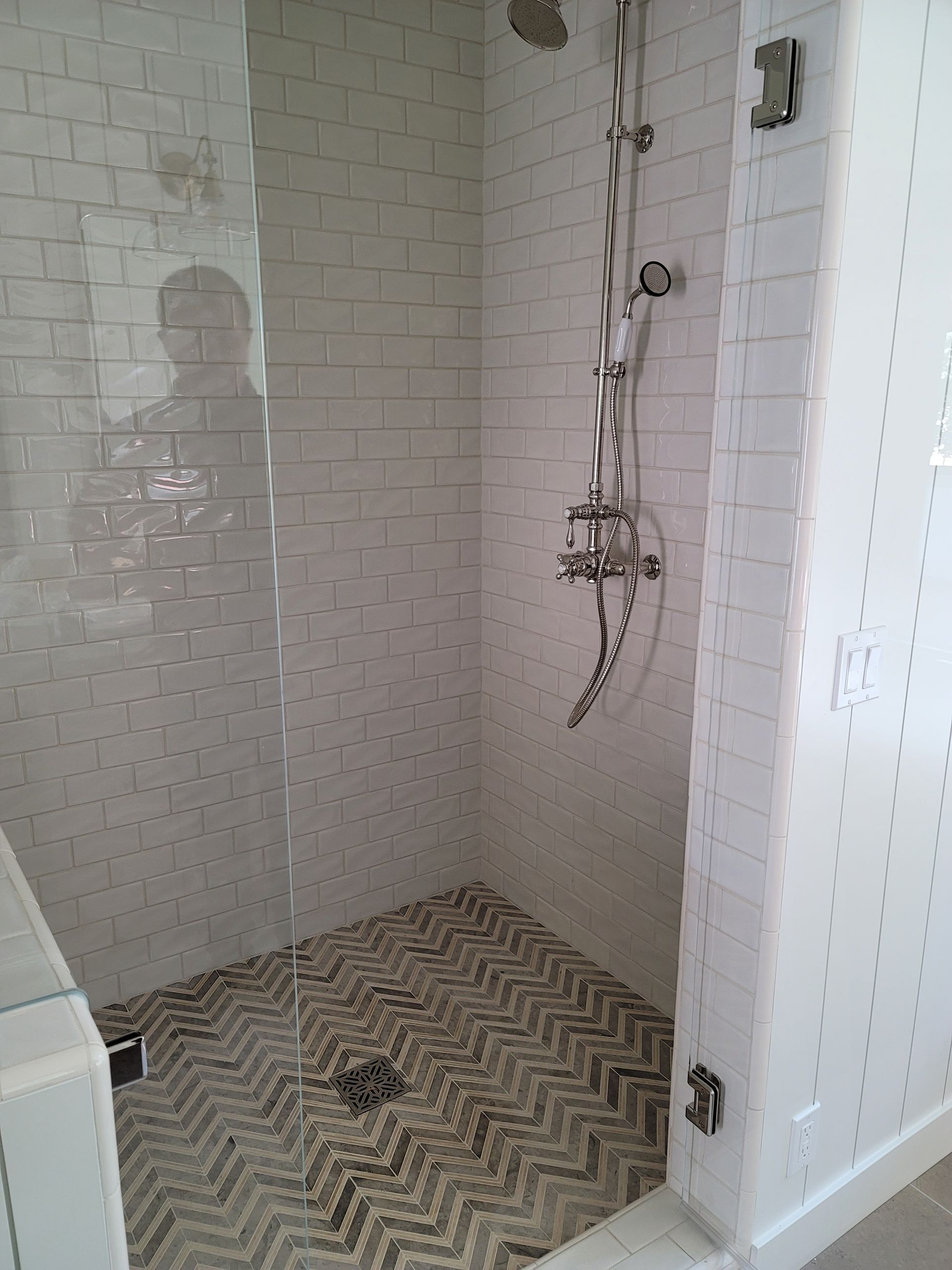Empty tiled shower stall with chrome fixtures and herringbone floor tile.