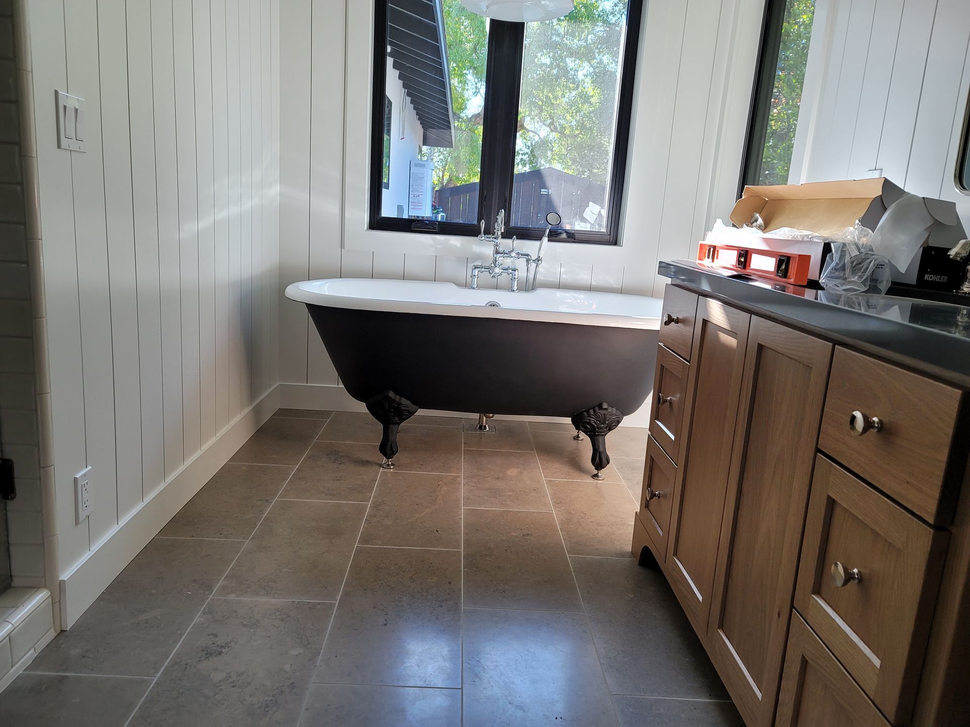 Bathroom with black clawfoot tub, window, white walls, and wood vanity on tiled floor