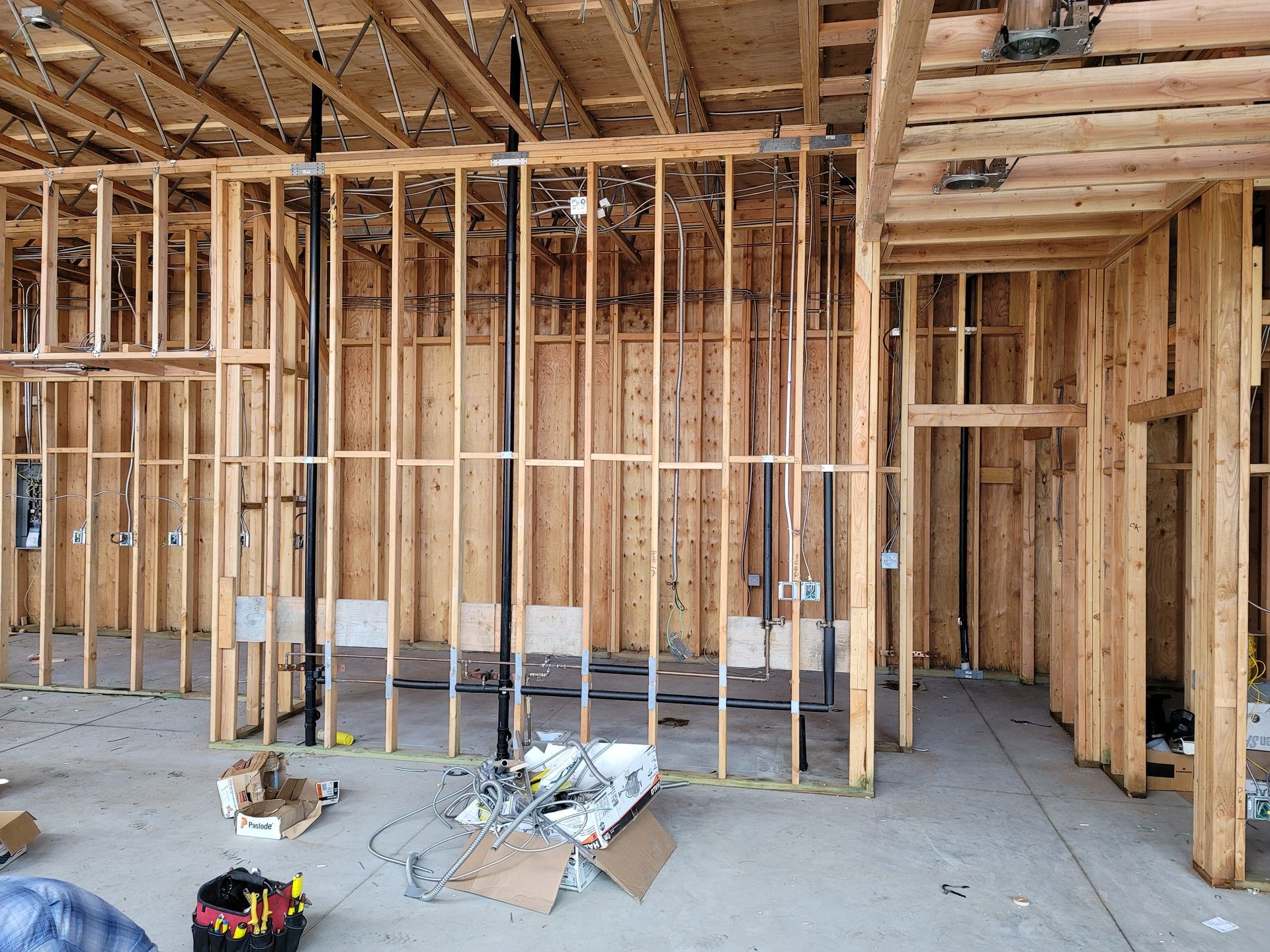 Unfinished house interior with exposed wooden framing, drywall debris, and concrete floor.