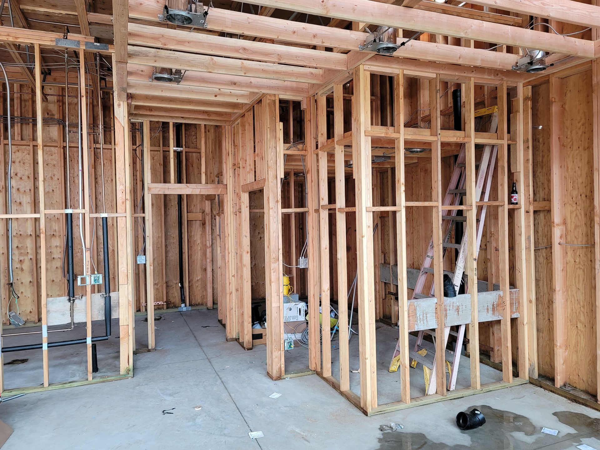 Unfinished house interior with exposed wooden framing and concrete floor during construction