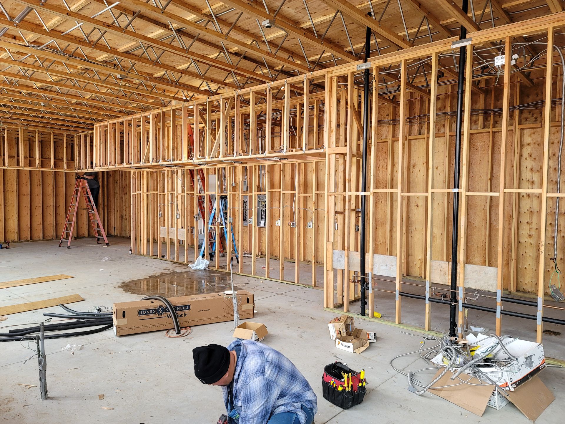 Interior of a house under construction with exposed wood framing, tools, and workers on the floor