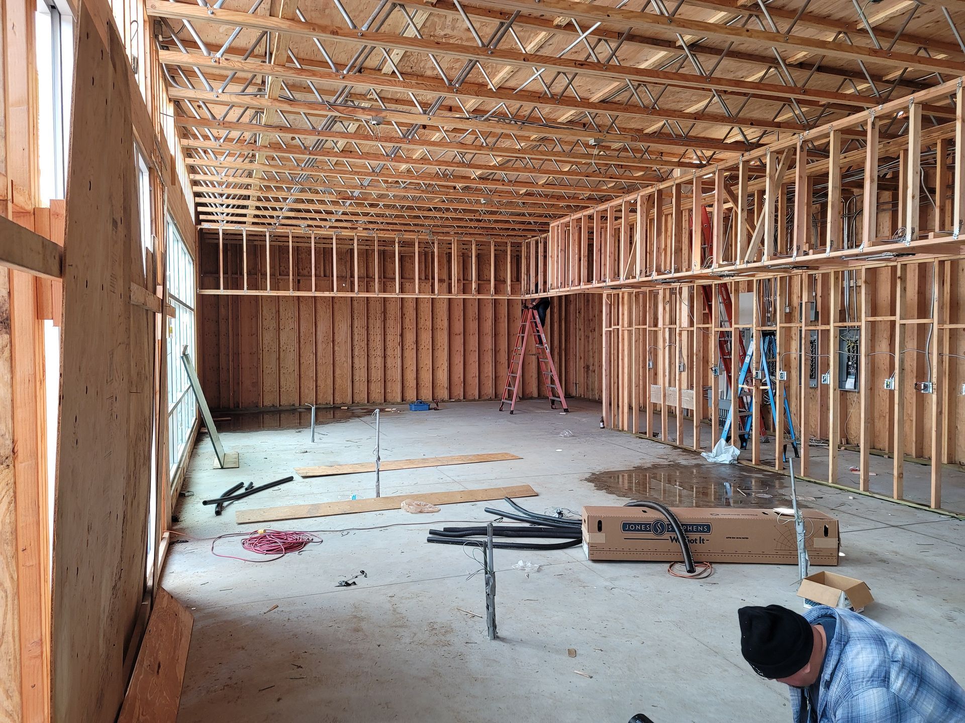Interior of a framed house under construction with exposed wooden studs and ceiling joists, tools on the floor.