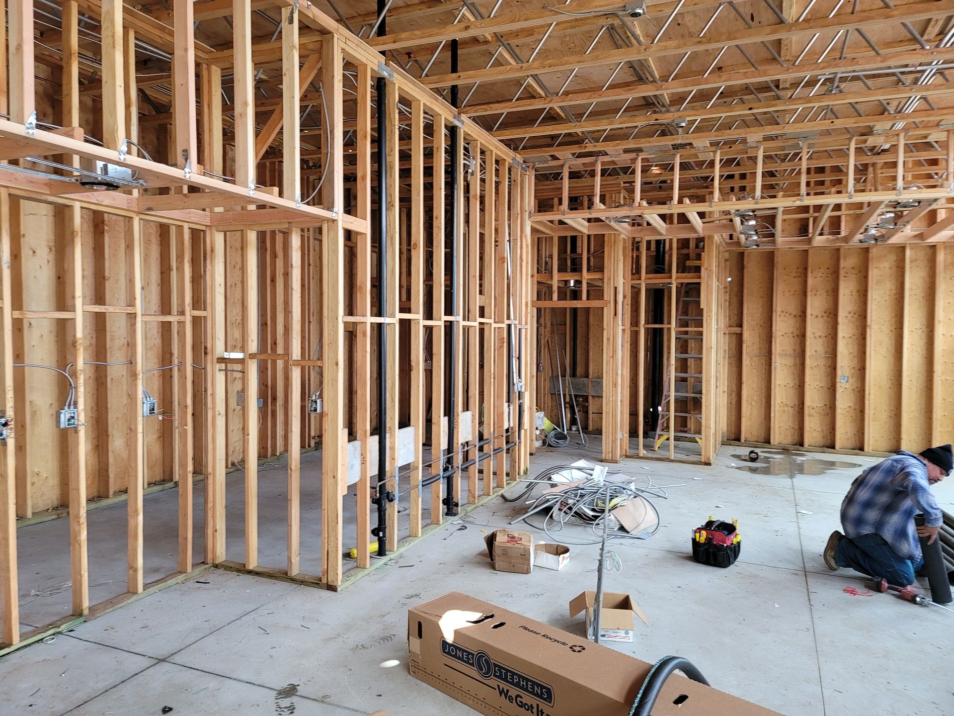 Framing of unfinished house interior with exposed wood studs and a worker kneeling on the floor