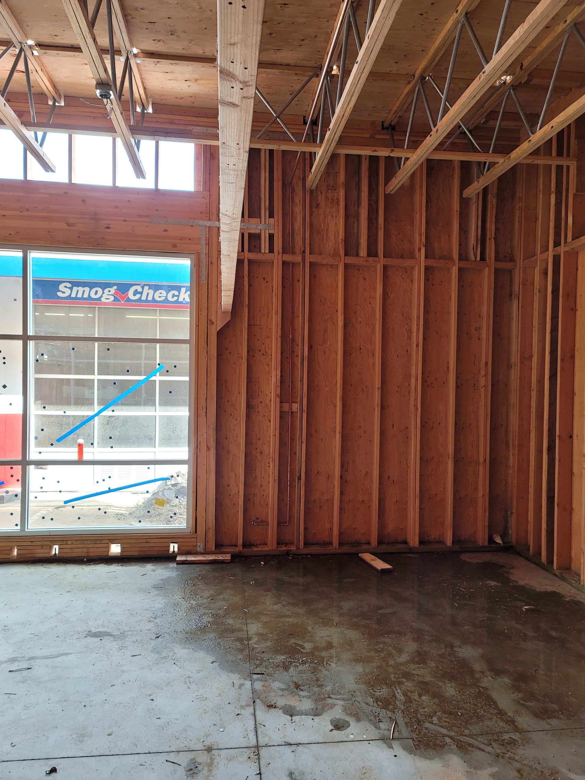 Unfinished room with exposed wood framing, concrete floor, and a window covered with blue tape.