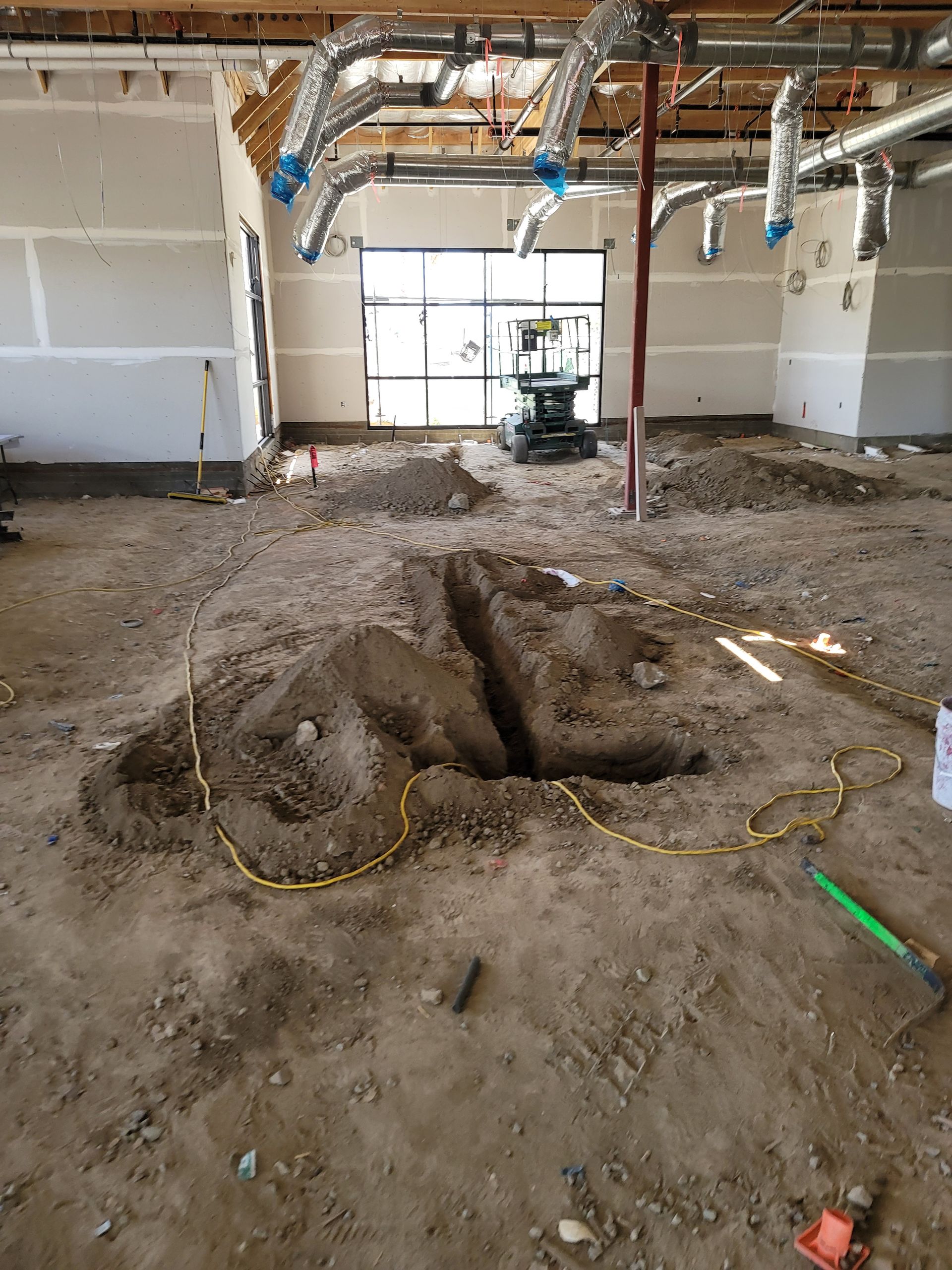 Interior construction site with exposed ceiling, debris, and a large dirt trench in the floor