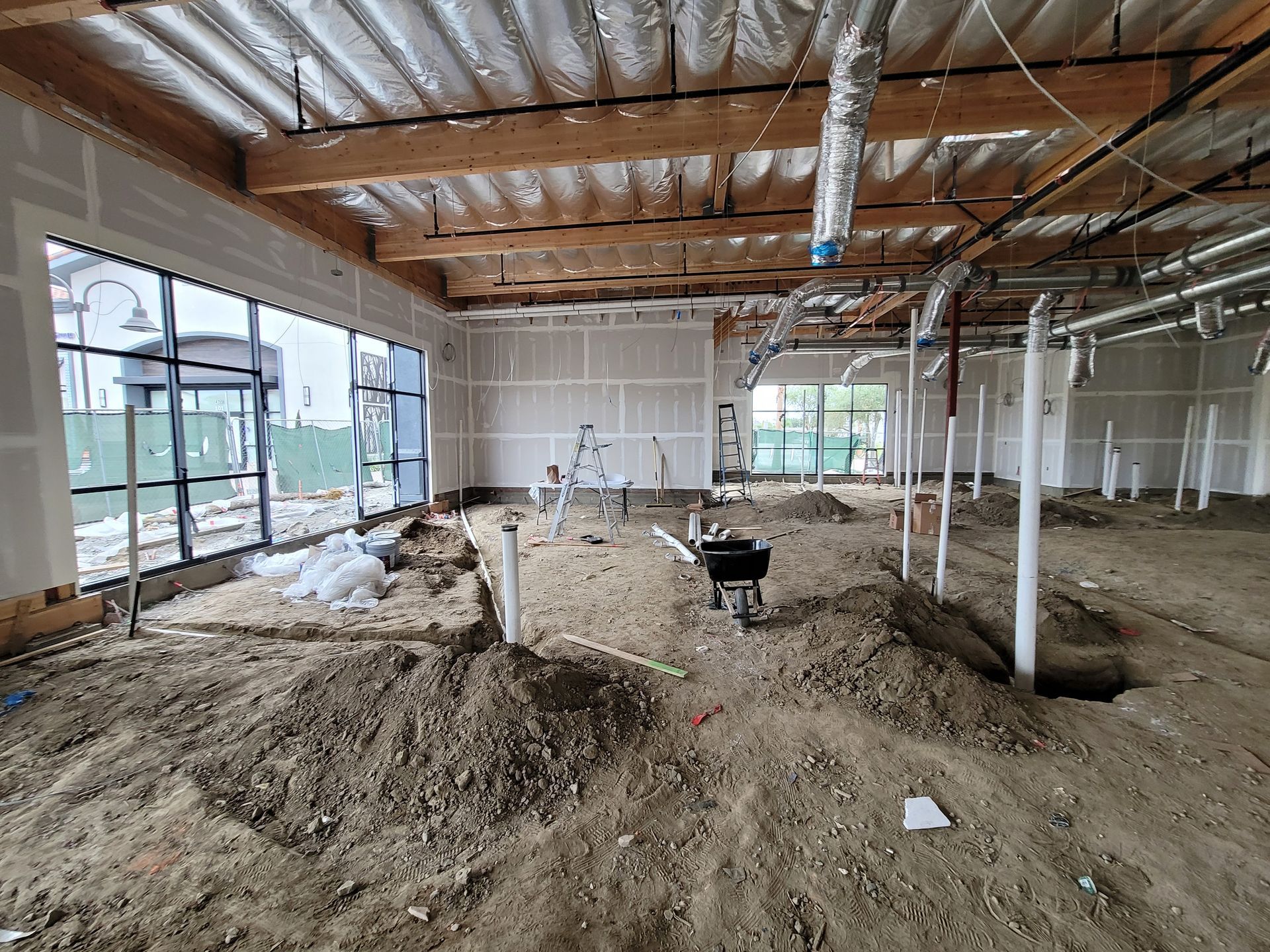 Interior of a building under construction with dirt mounds, exposed beams, and unfinished walls
