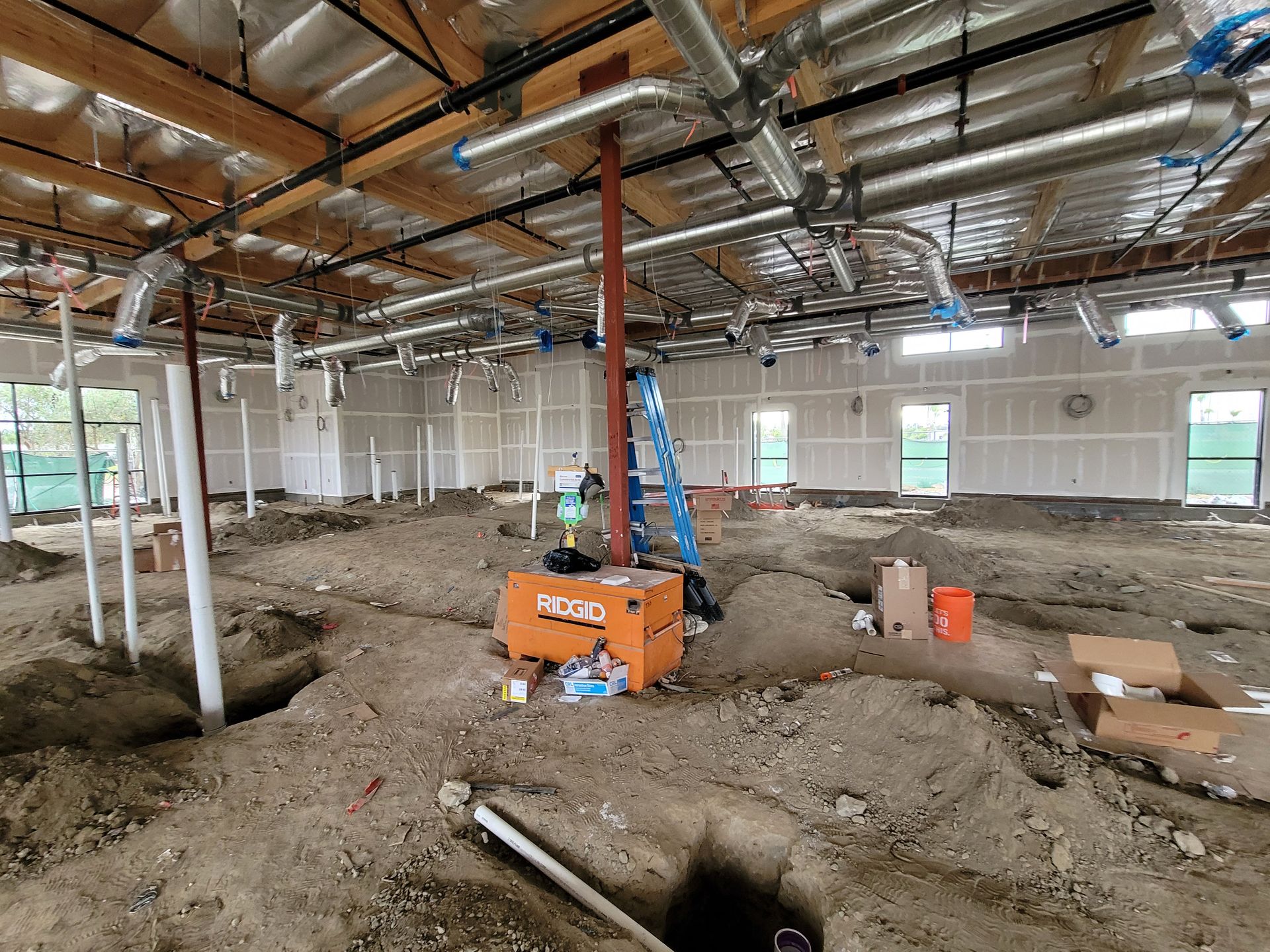 Construction site interior with exposed ceiling, dirt floor, and a blue lift near orange equipment