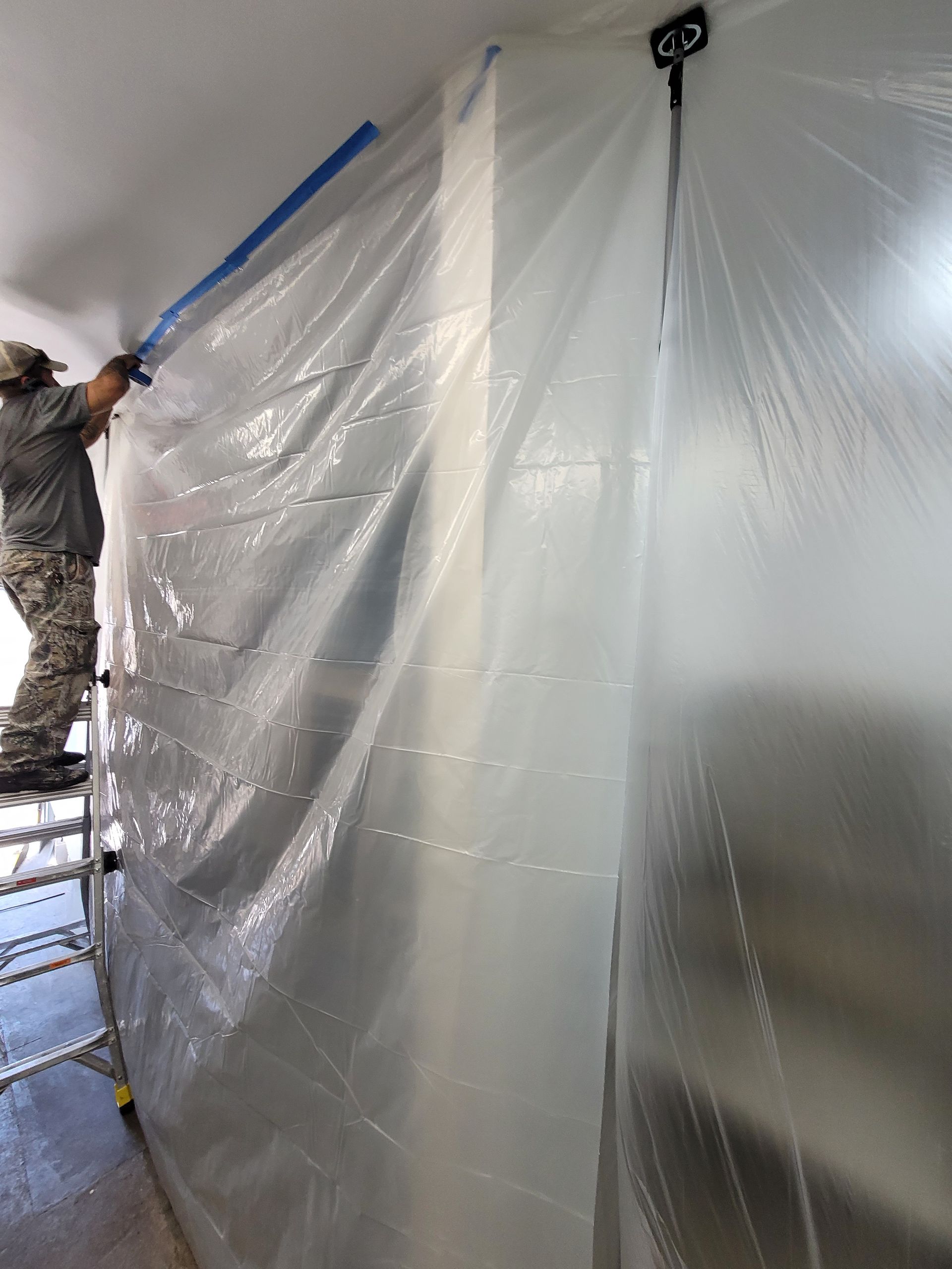 Worker hanging clear plastic sheeting over a room doorway during renovation