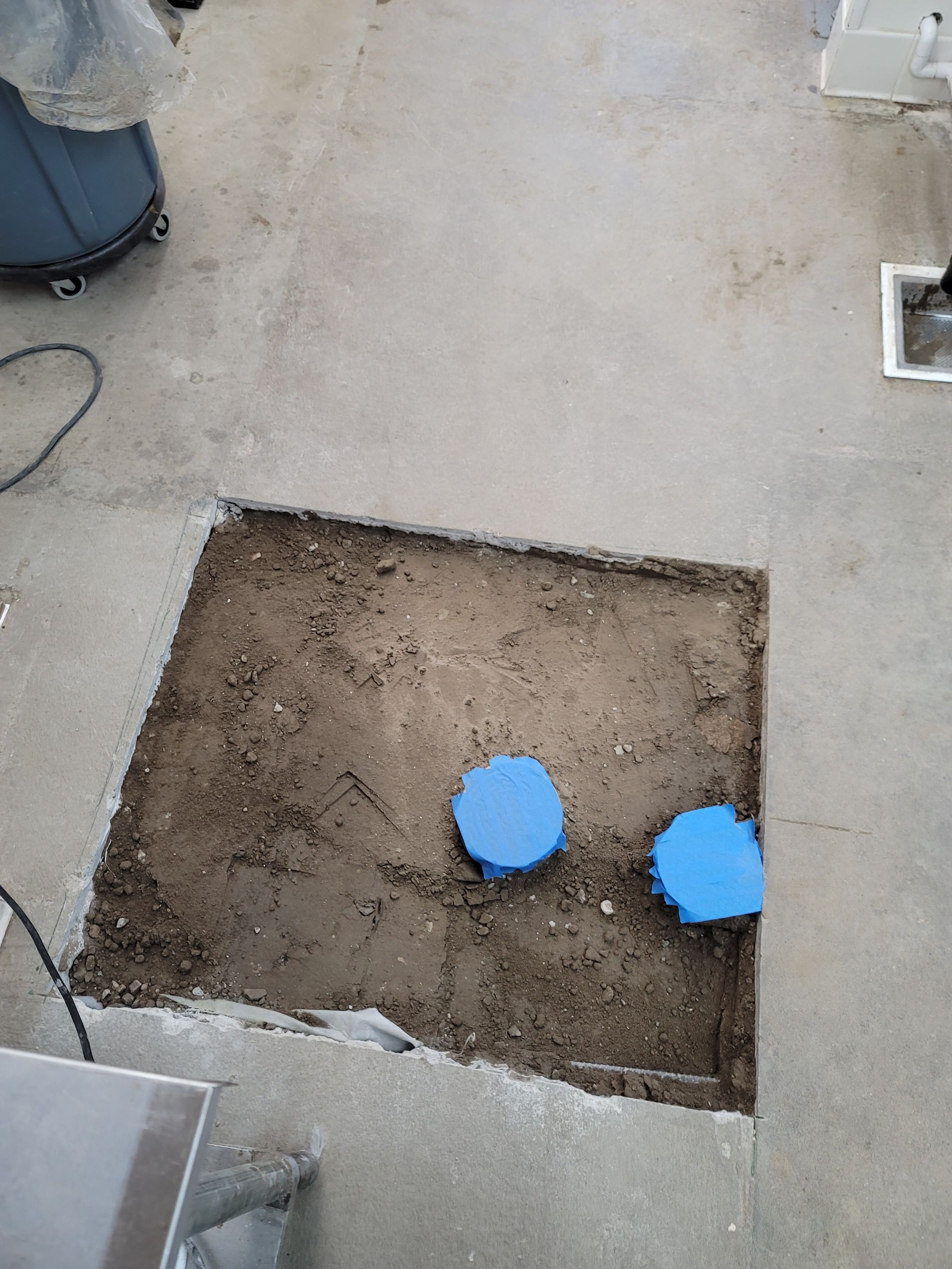 Outdoor concrete slab with a square dirt cutout and two blue caps or covers inside
