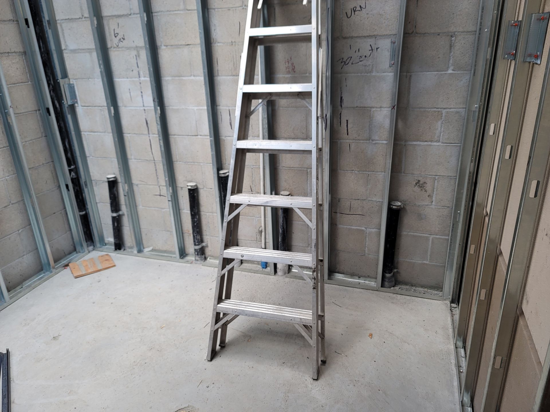Aluminum ladder standing in an unfinished room with concrete walls and floor.