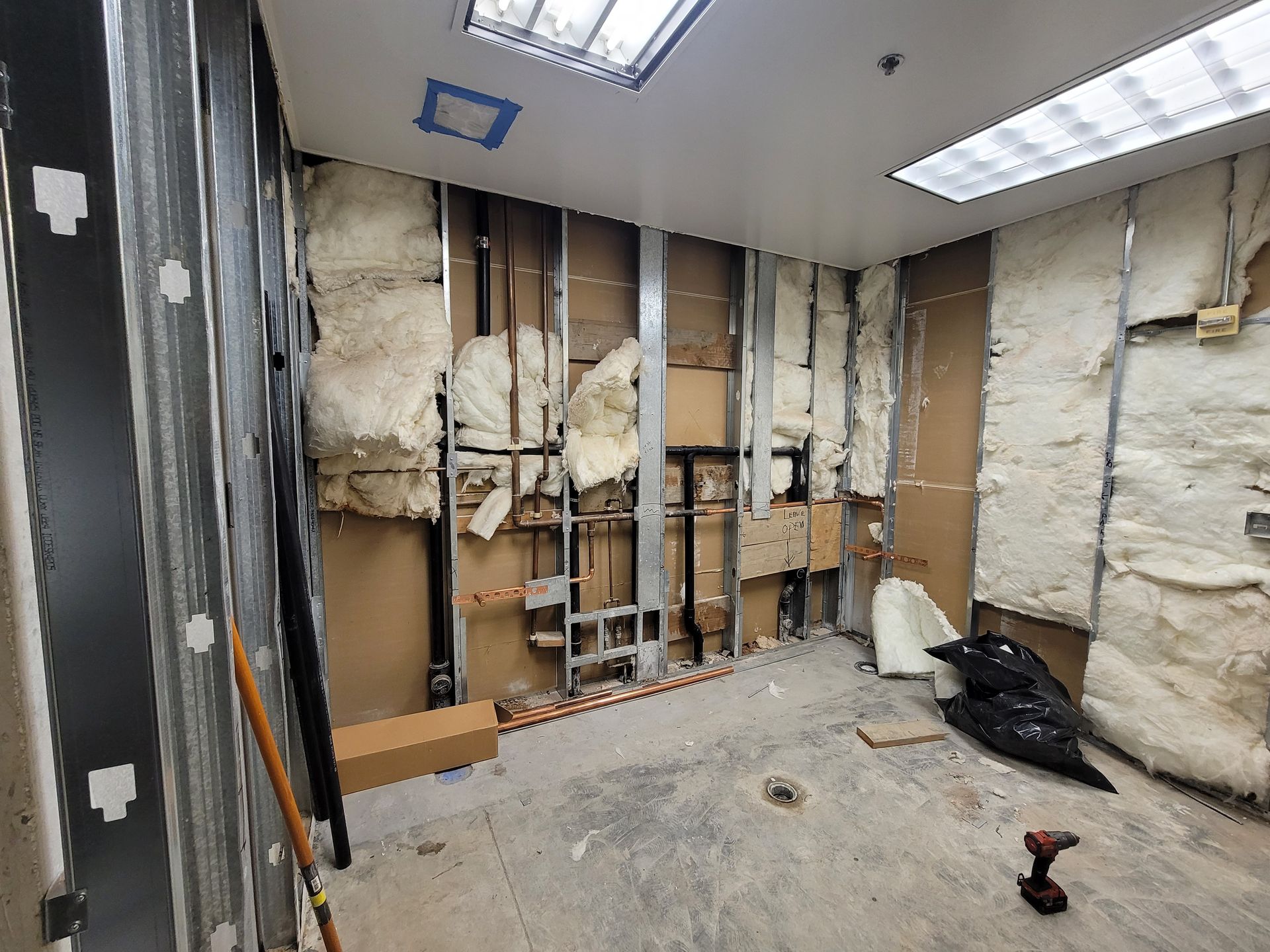 Partially demolished room with exposed studs, insulation, and debris under fluorescent lights