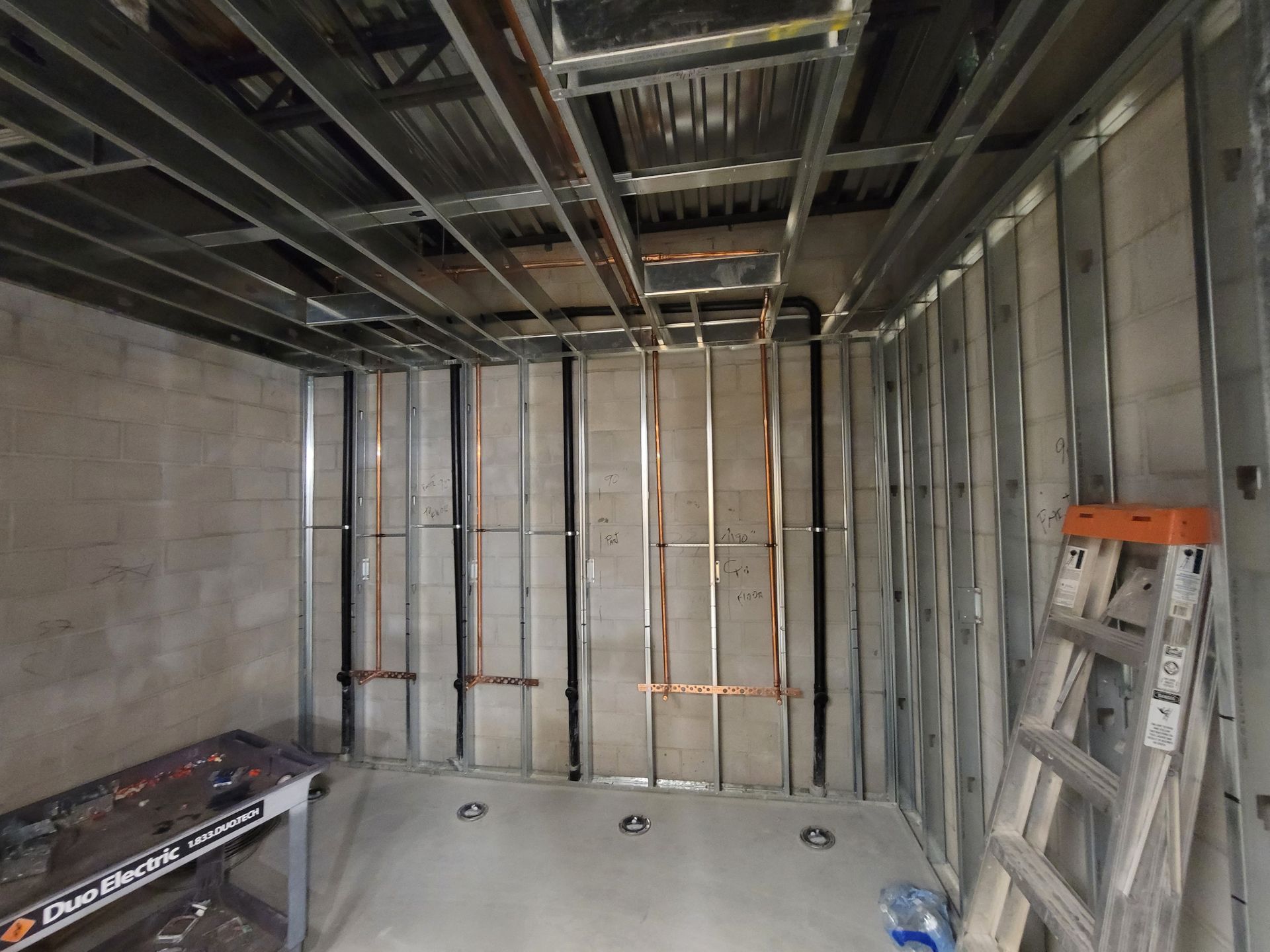 Unfinished room with exposed metal framing, concrete floor, and a ladder leaning against the right wall.