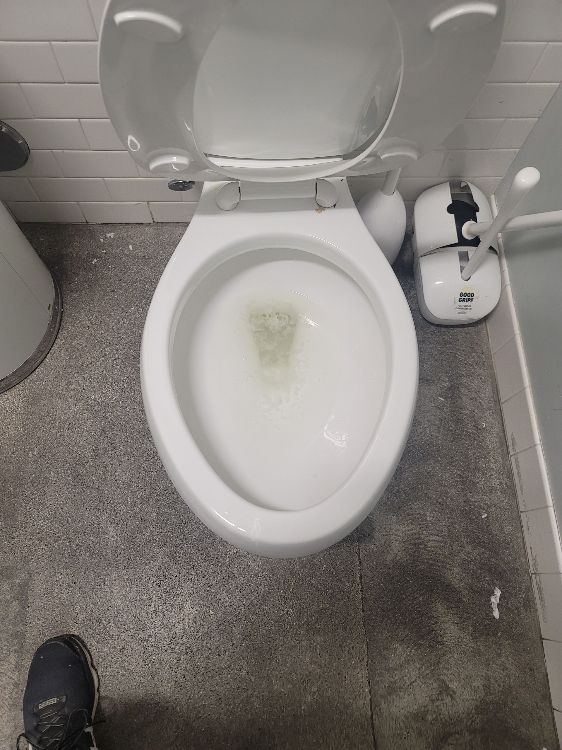 Top-down view of a toilet in a restroom with the seat up and a yellow stain in the bowl.