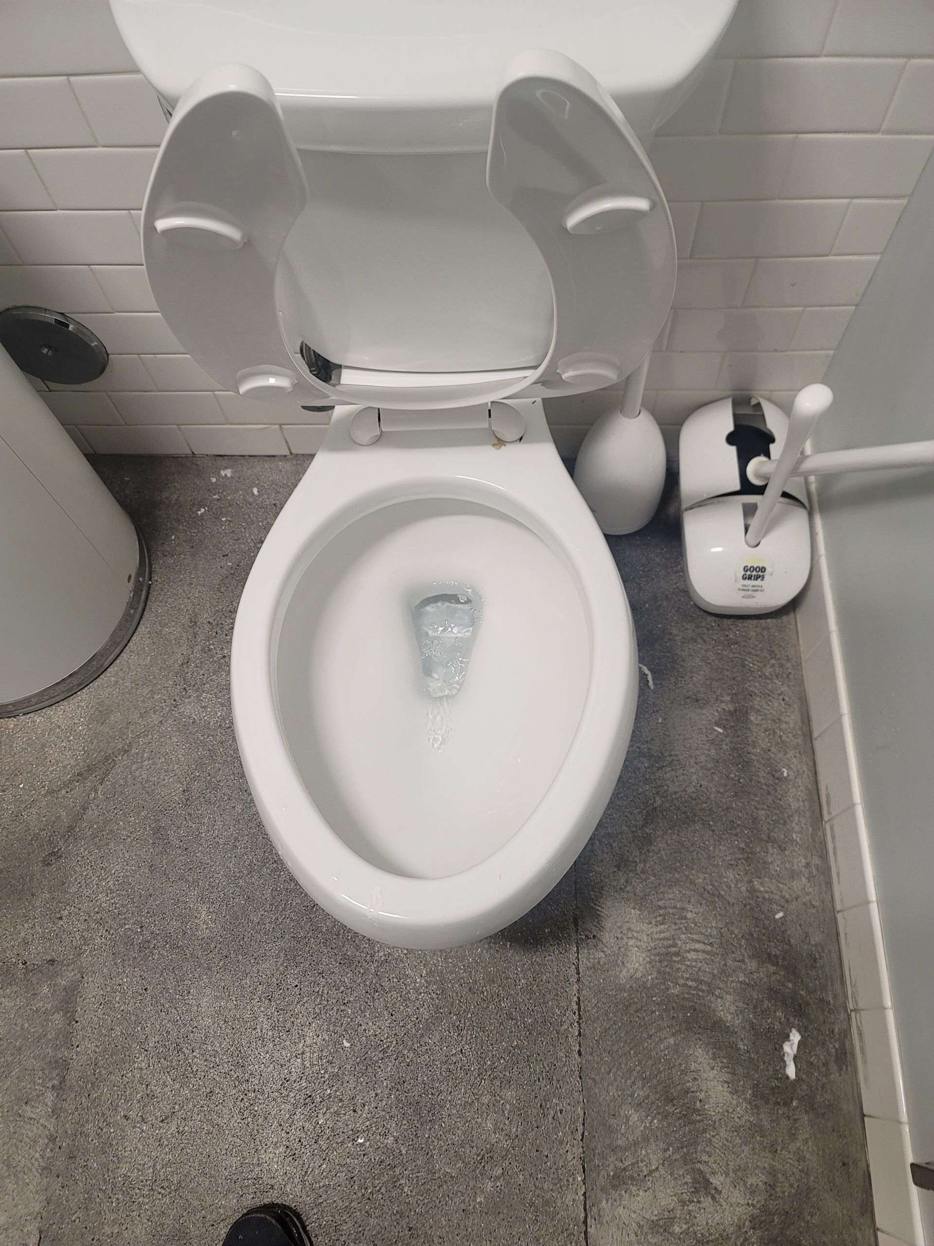 Small bathroom with a toilet, white seat cover, and cleaning supplies beside it.