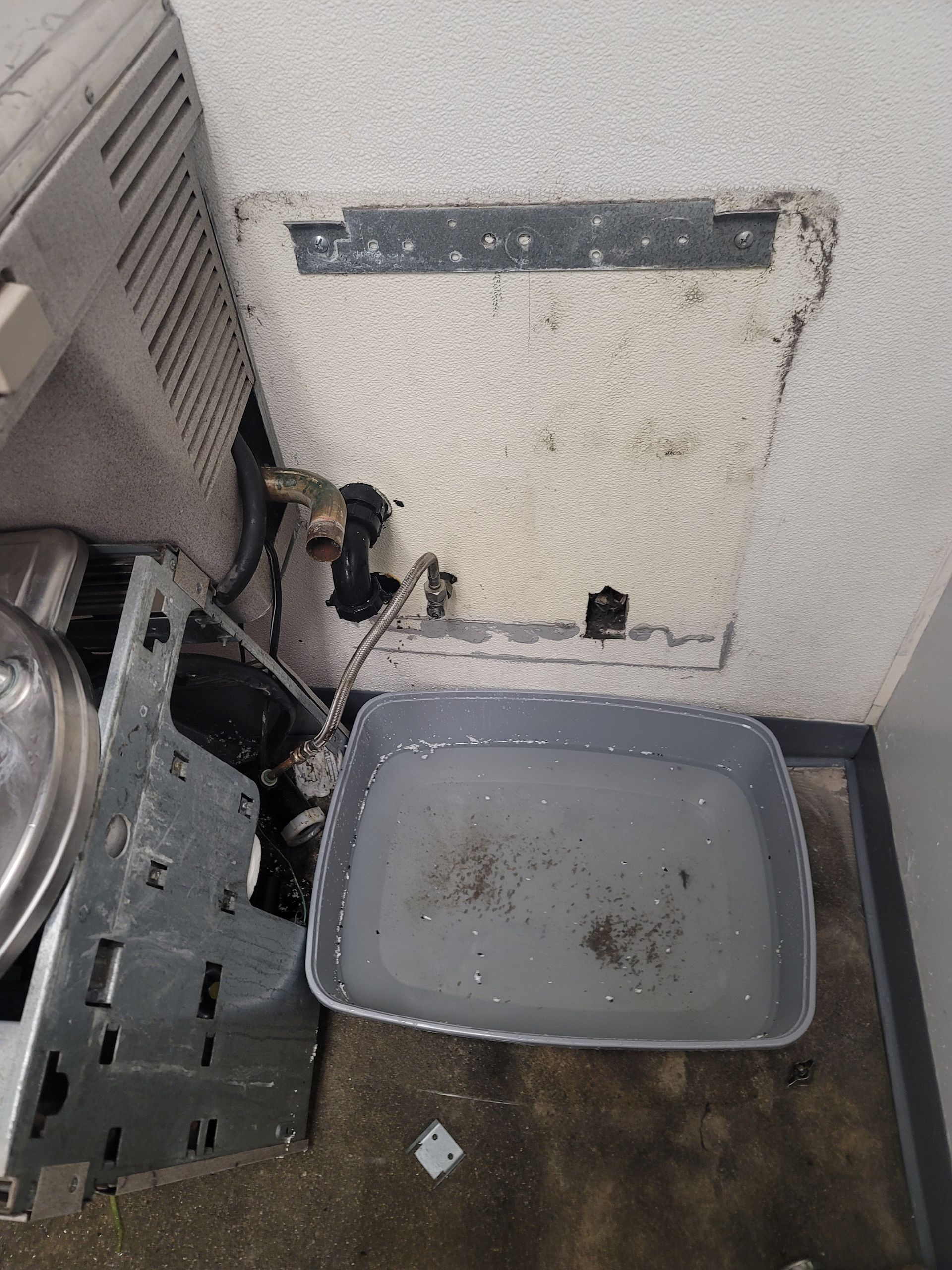 Messy utility corner with a gray bin, exposed wall panel, and scattered debris on the floor