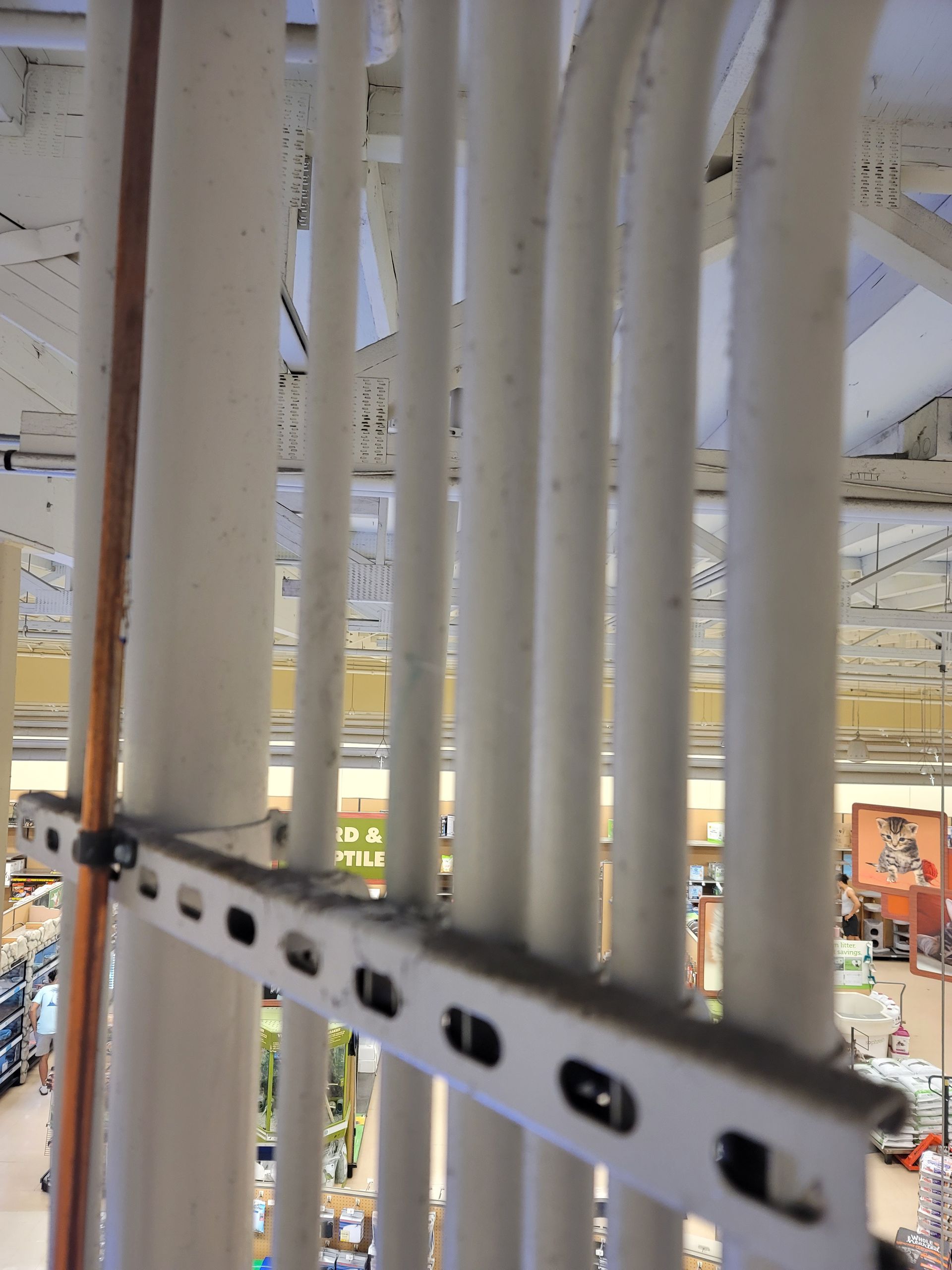 Metal beams and white pipes inside an industrial ceiling structure, viewed from a high vantage point