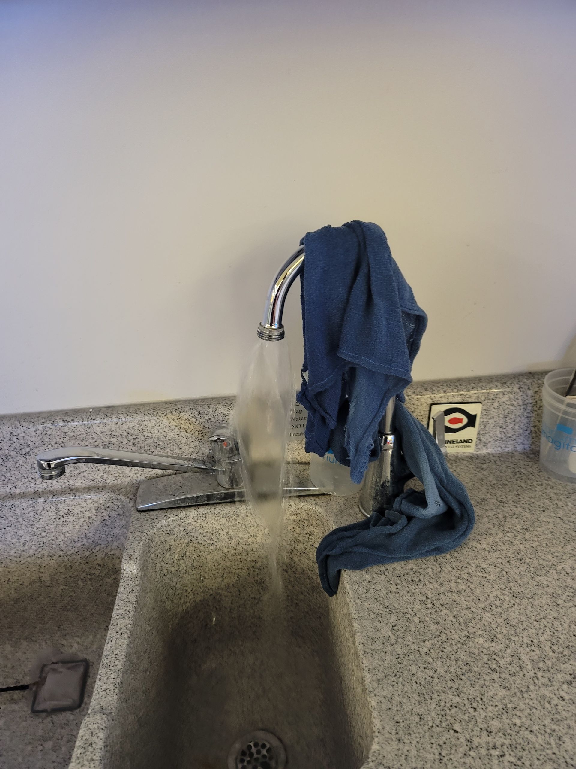 Sink with running water and a blue cloth draped over the faucet in a speckled countertop restroom.