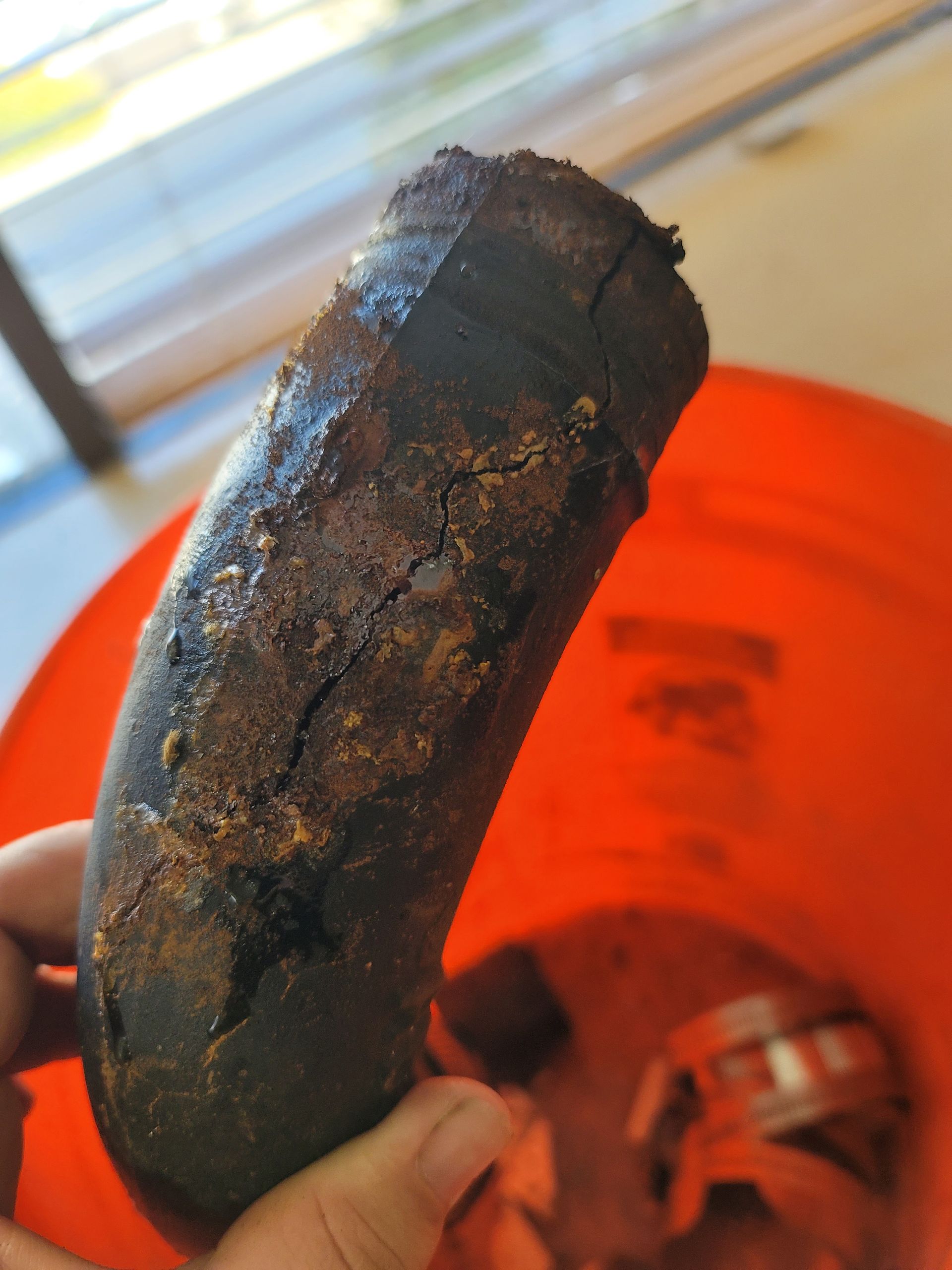 A blackened, burnt object held over an orange bucket indoors.