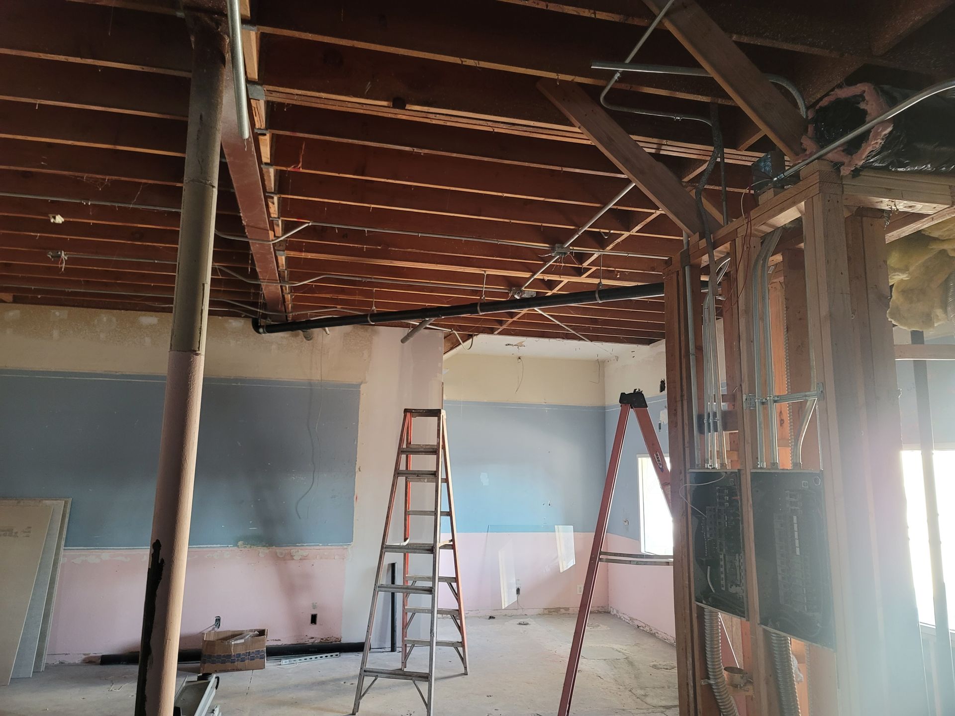 Renovation site with exposed wooden ceiling, ladders, and unfinished walls in a room under construction