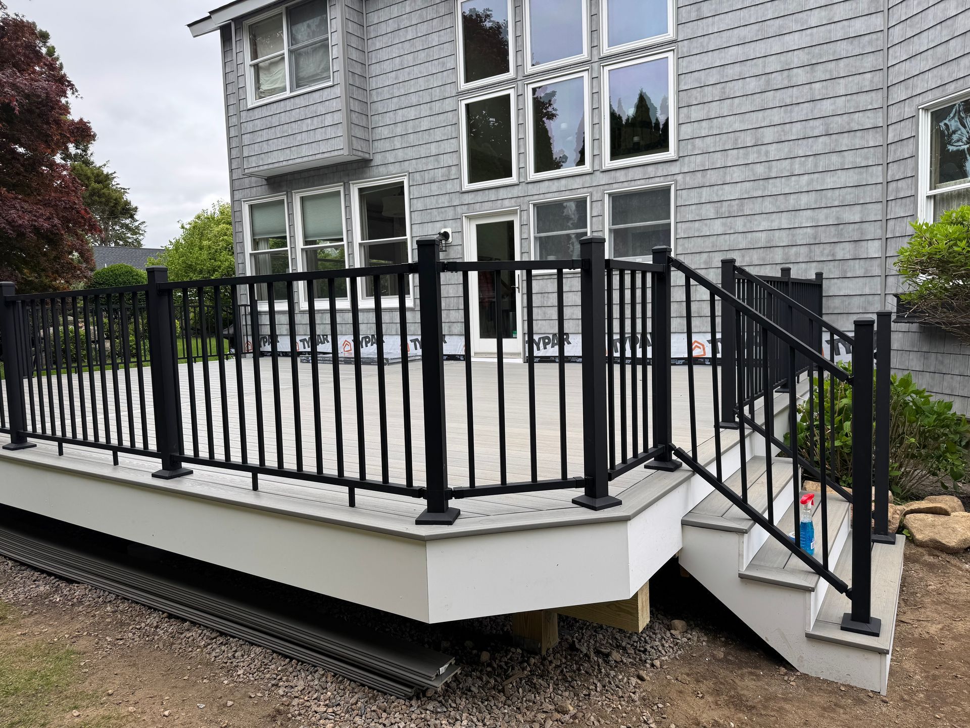 A light gray deck with black metal railings and a staircase, attached to the back of a house with light gray shingles.