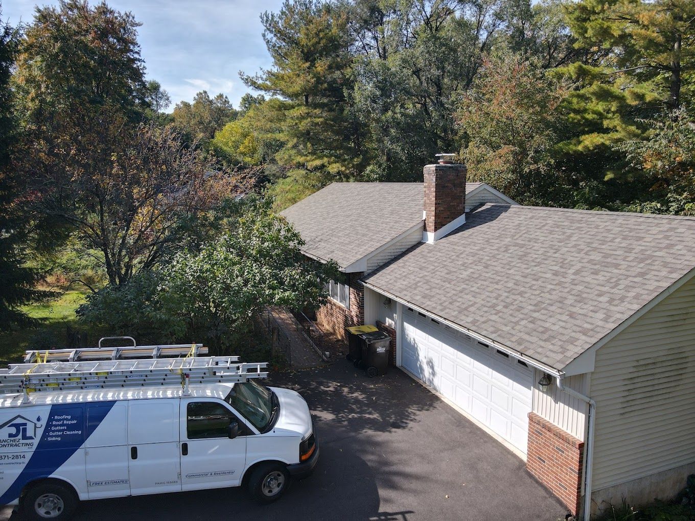 A white van with a ladder on top is parked in front of a house