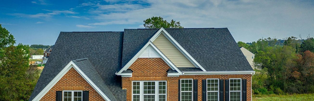 A large brick house with a black roof is sitting in the middle of a field.