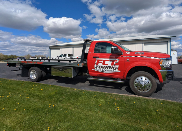 Red tow truck on a road beside a grassy field under a cloudy sky