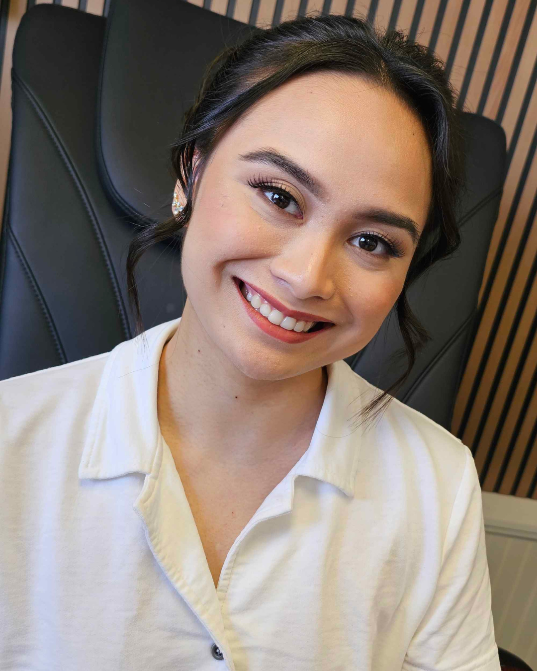 Woman with styled dark hair, light makeup, smiling in white shirt.