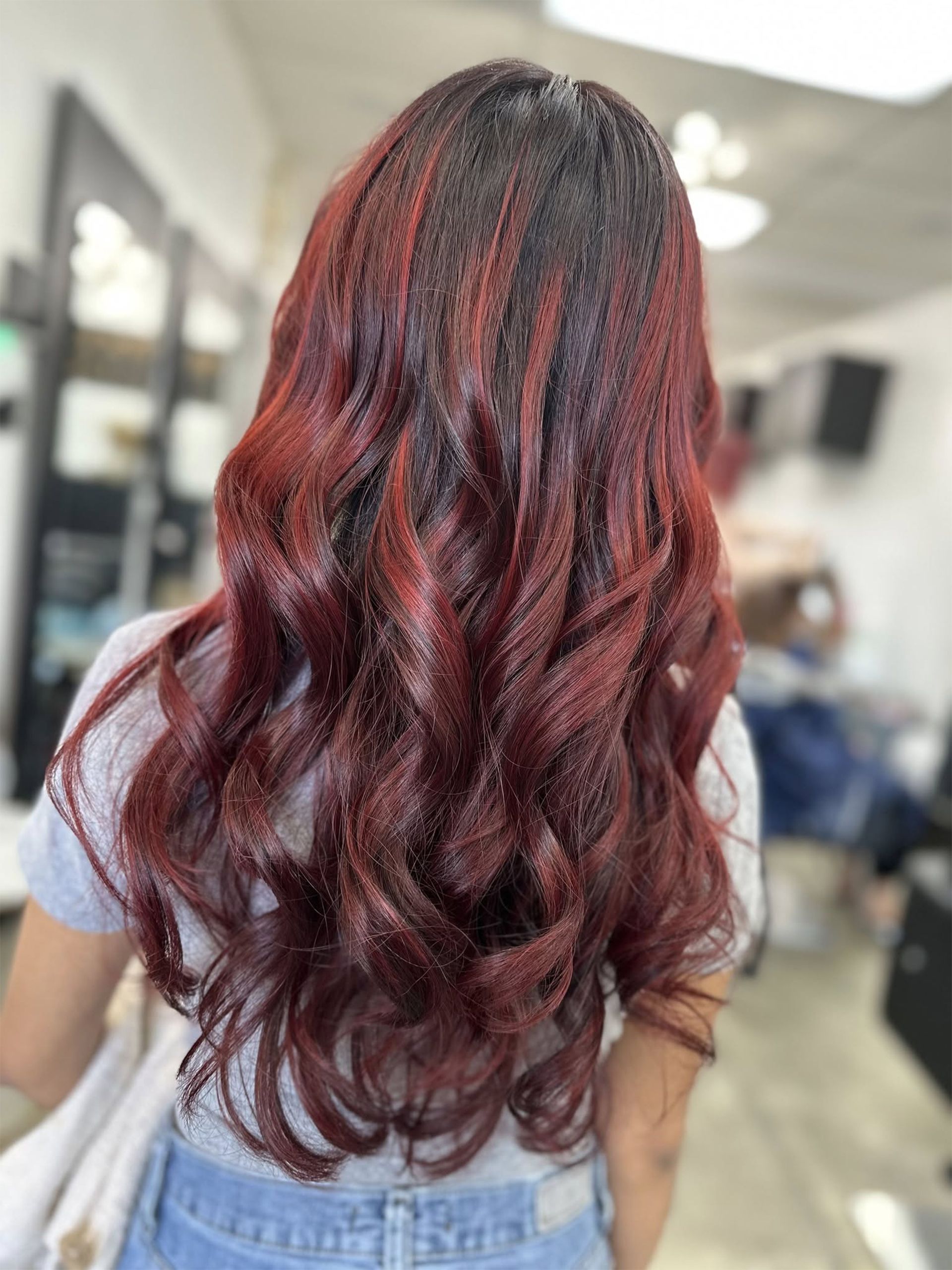 Woman with long, wavy auburn hair. Salon setting with light in the background.
